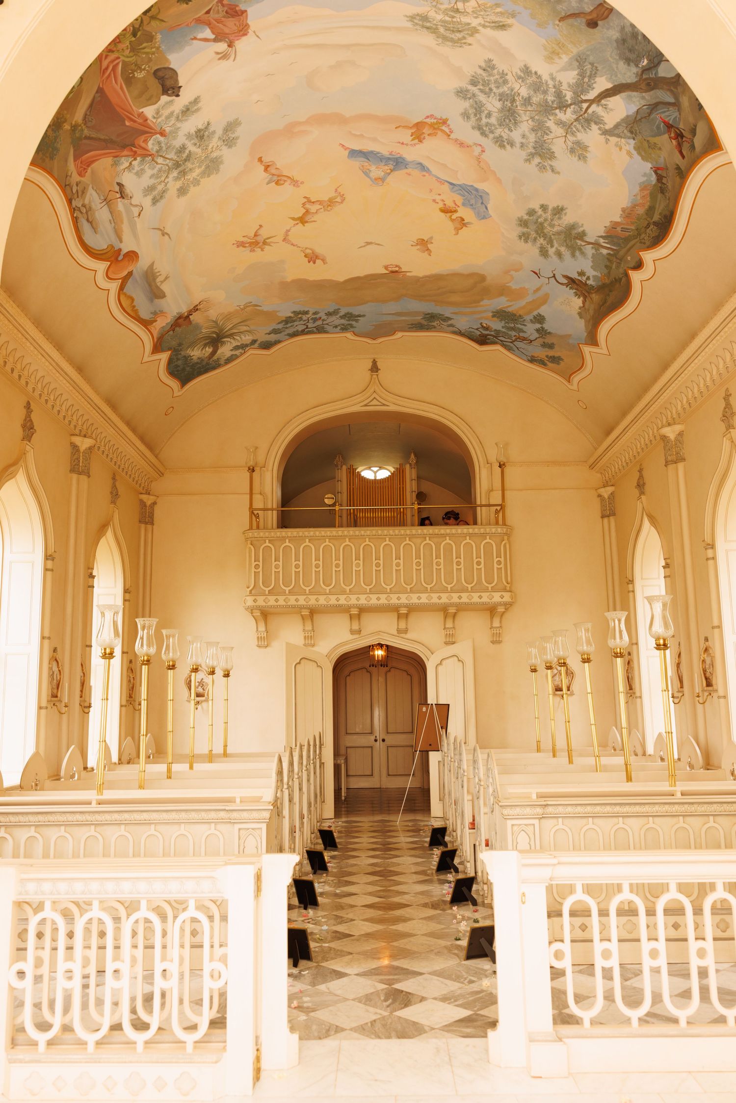 Elegant church interior with ornate ceiling fresco, white balustrades and balcony featuring classical architectural details.
