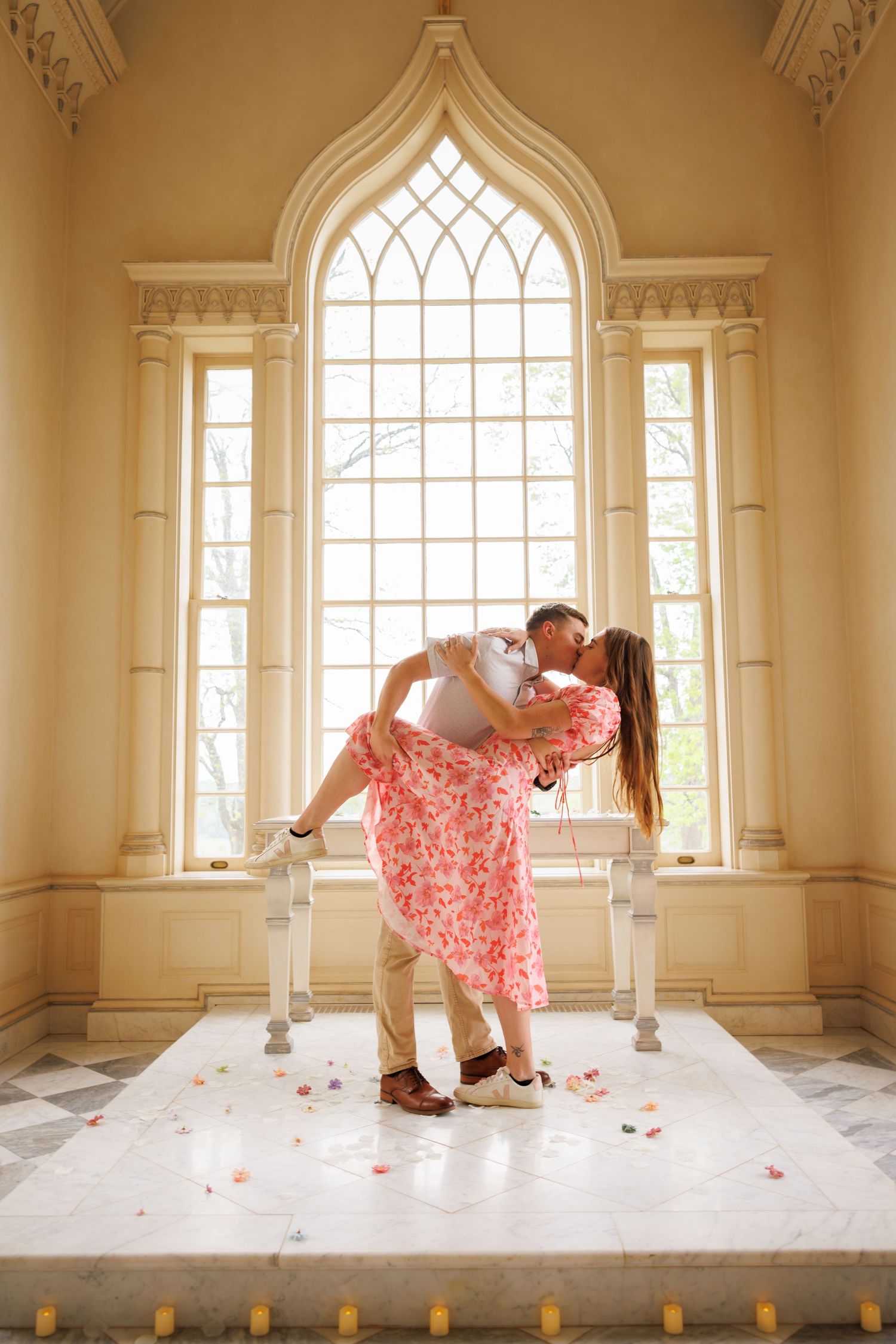 A romantic moment in front of a gothic church window with rose petals scattered on a white platform.