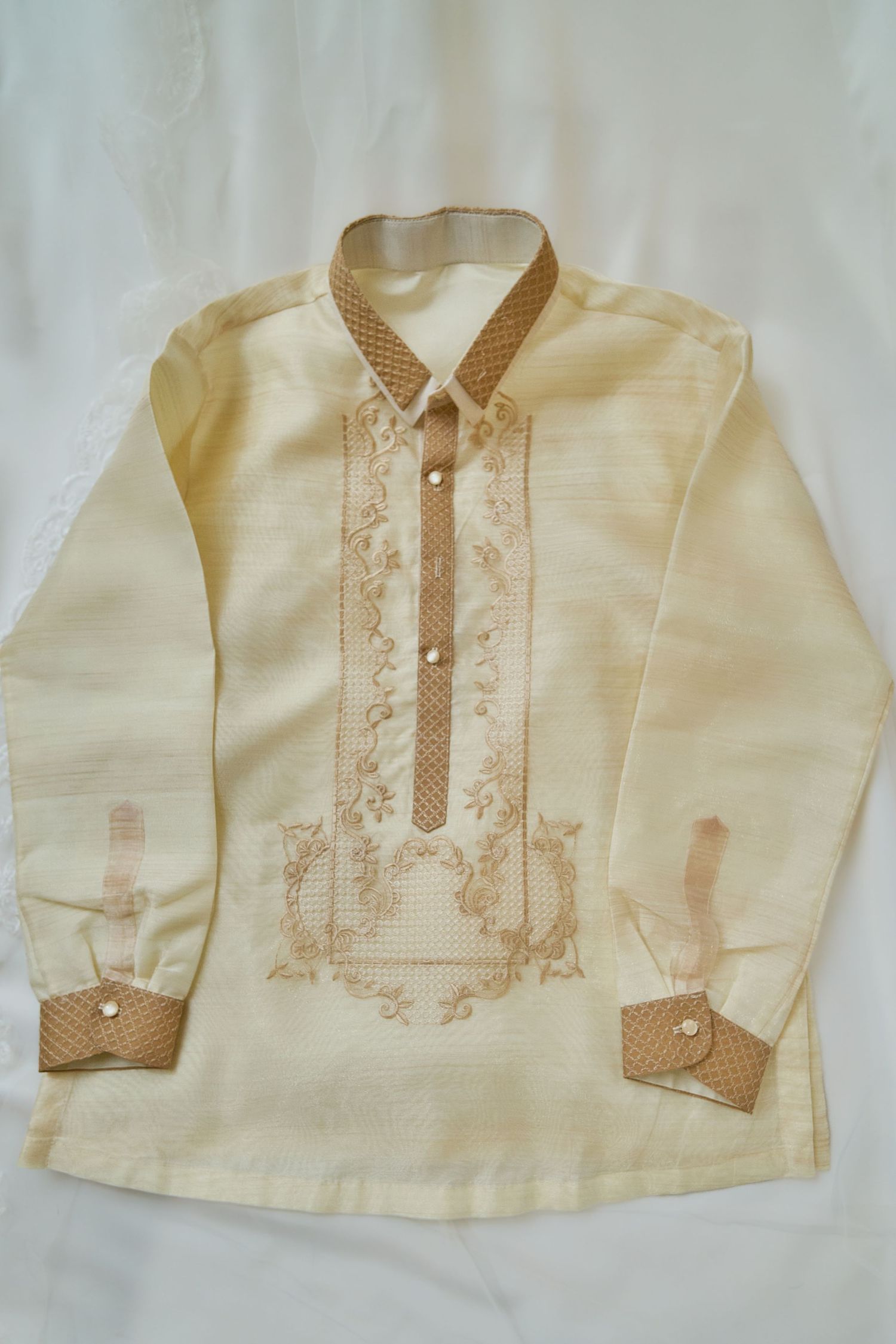 Traditional cream colored Barong Tagalog with intricate embroidered details on the front and brown polka dot accents.