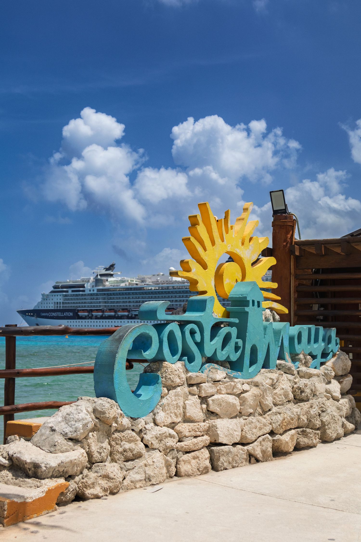 Decorative welcome sign with sun motif on stone wall at tropical beach with cruise ship in background.
