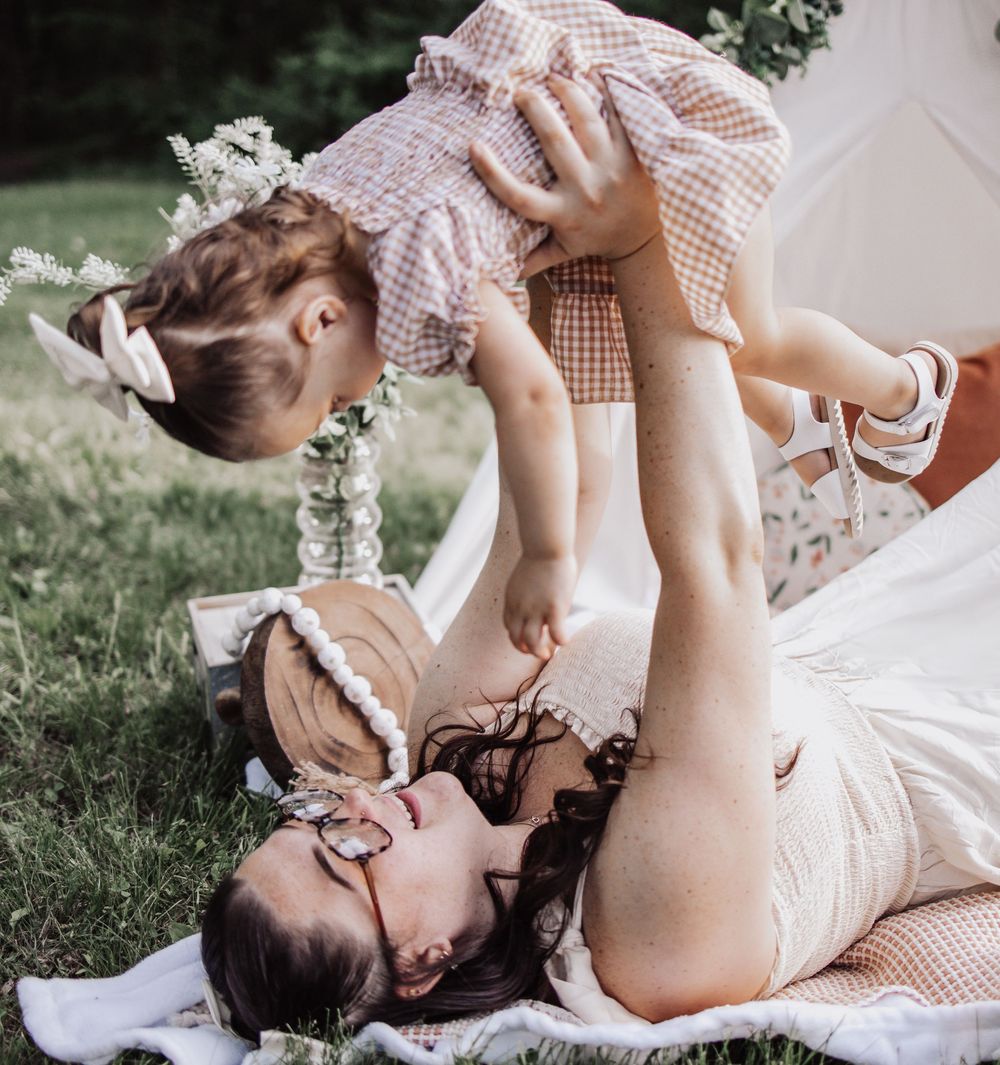 Sweet moment captured outdoors on a blanket with gingham dresses and playful cuddles in the summer grass.