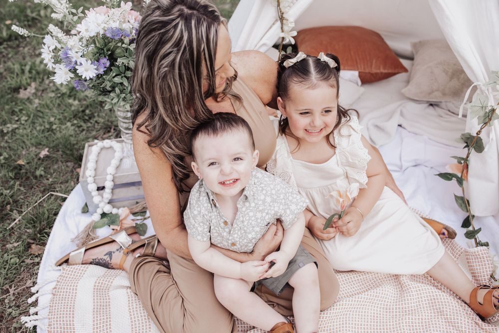 Family enjoying a picnic together on a blanket outdoors with white decor and floral arrangements.