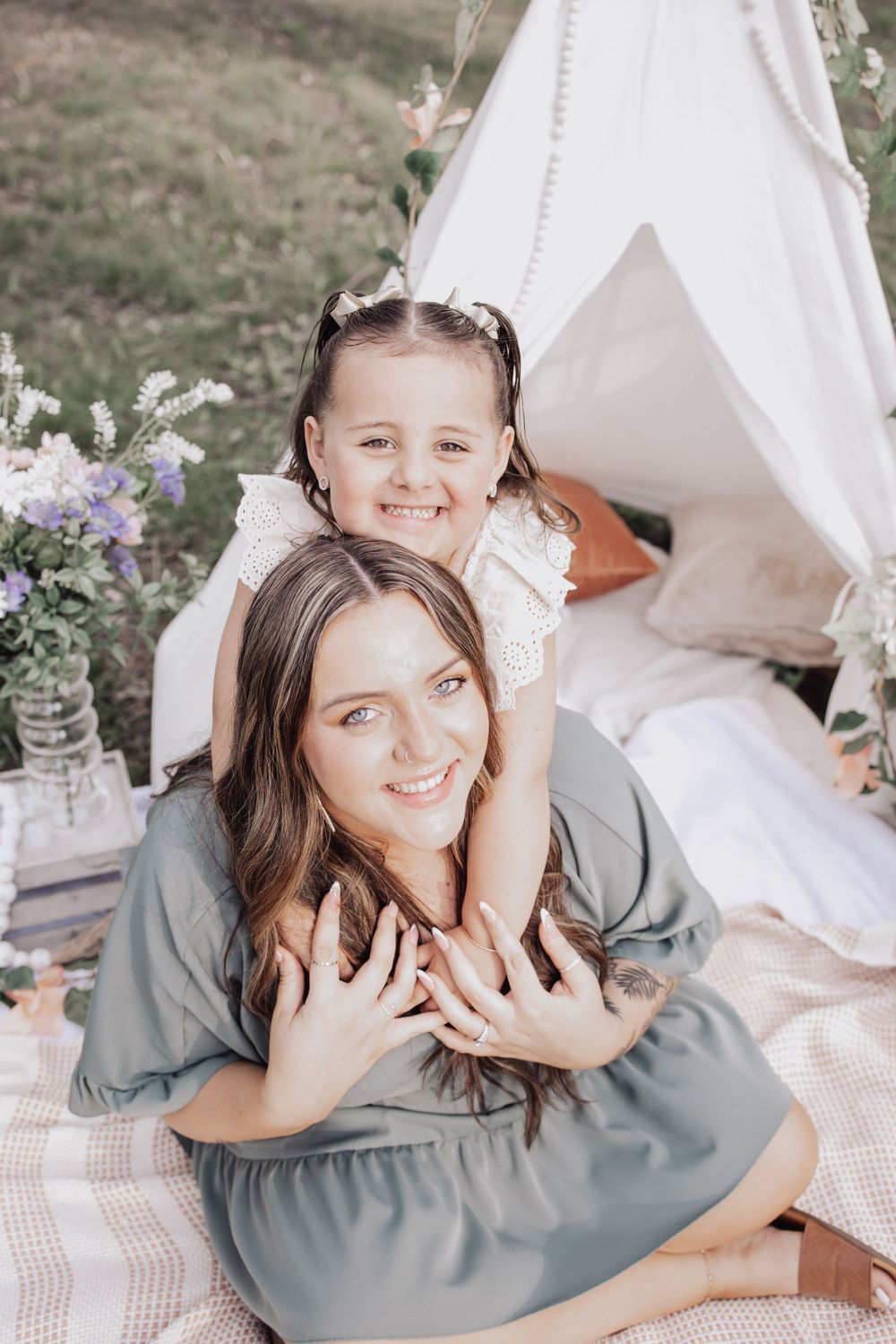A cozy outdoor picnic setup with a white teepee tent, striped blanket, and purple flowers in a vase.