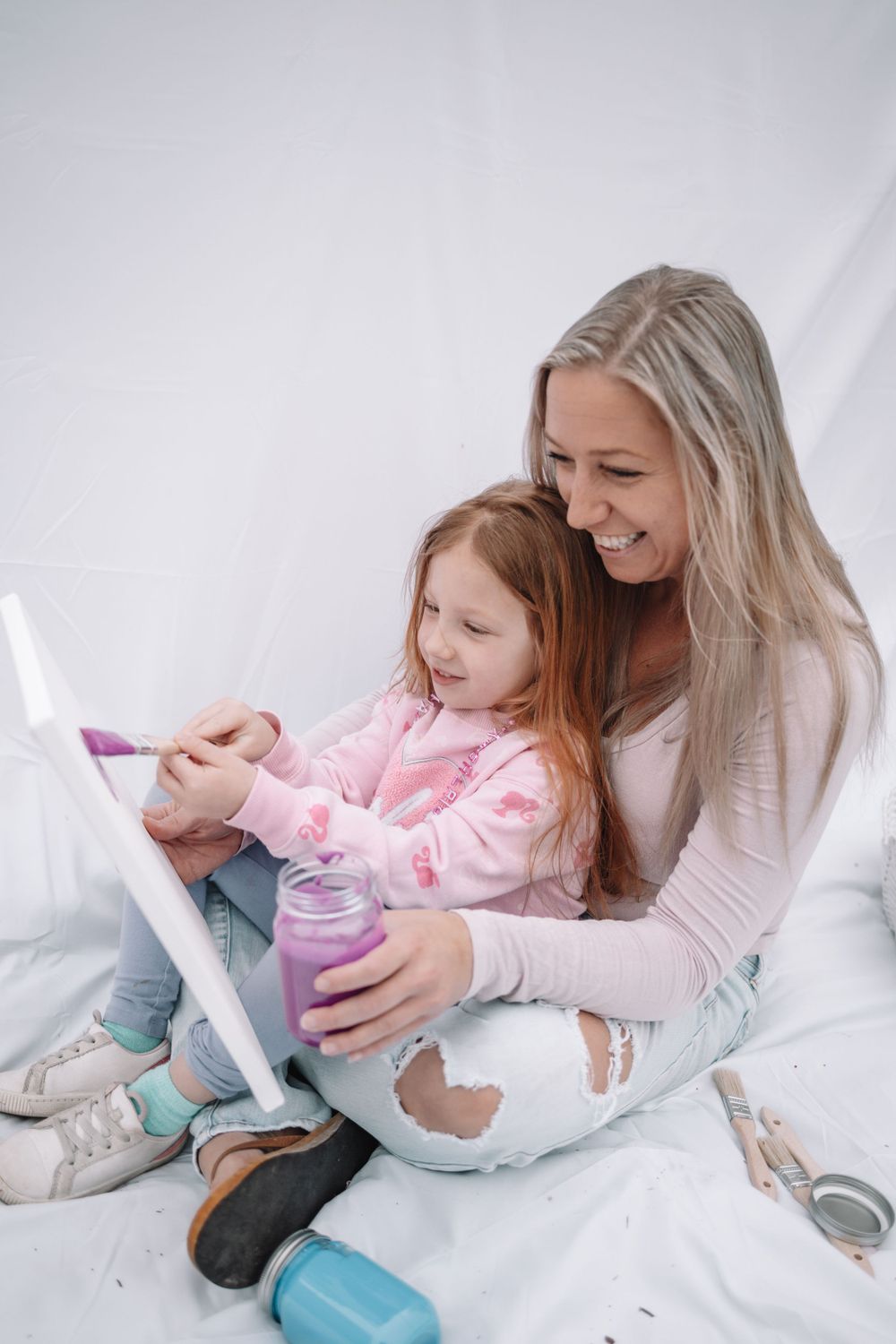 A joyful moment of bonding and reading together on white bedding with reusable water bottles nearby.