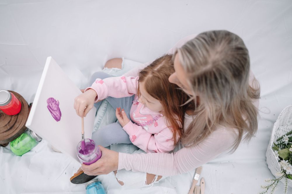 Adult and child sit together playing with colorful toys on white blanket during quality bonding time.