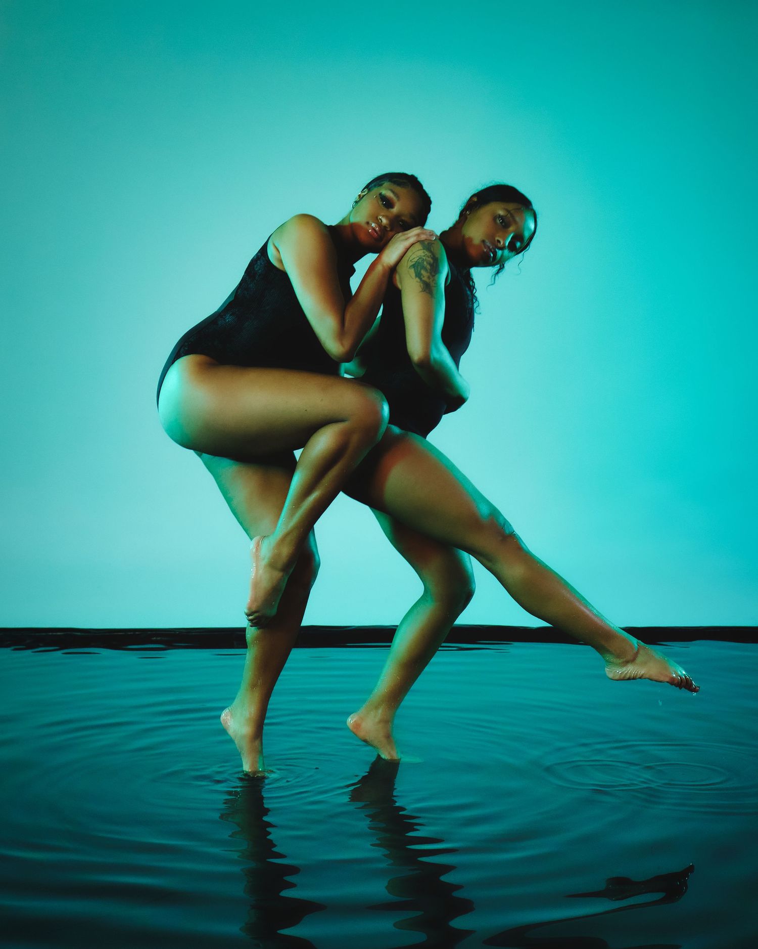 Contemporary dancers perform duet in blue-lit studio with water reflection.
