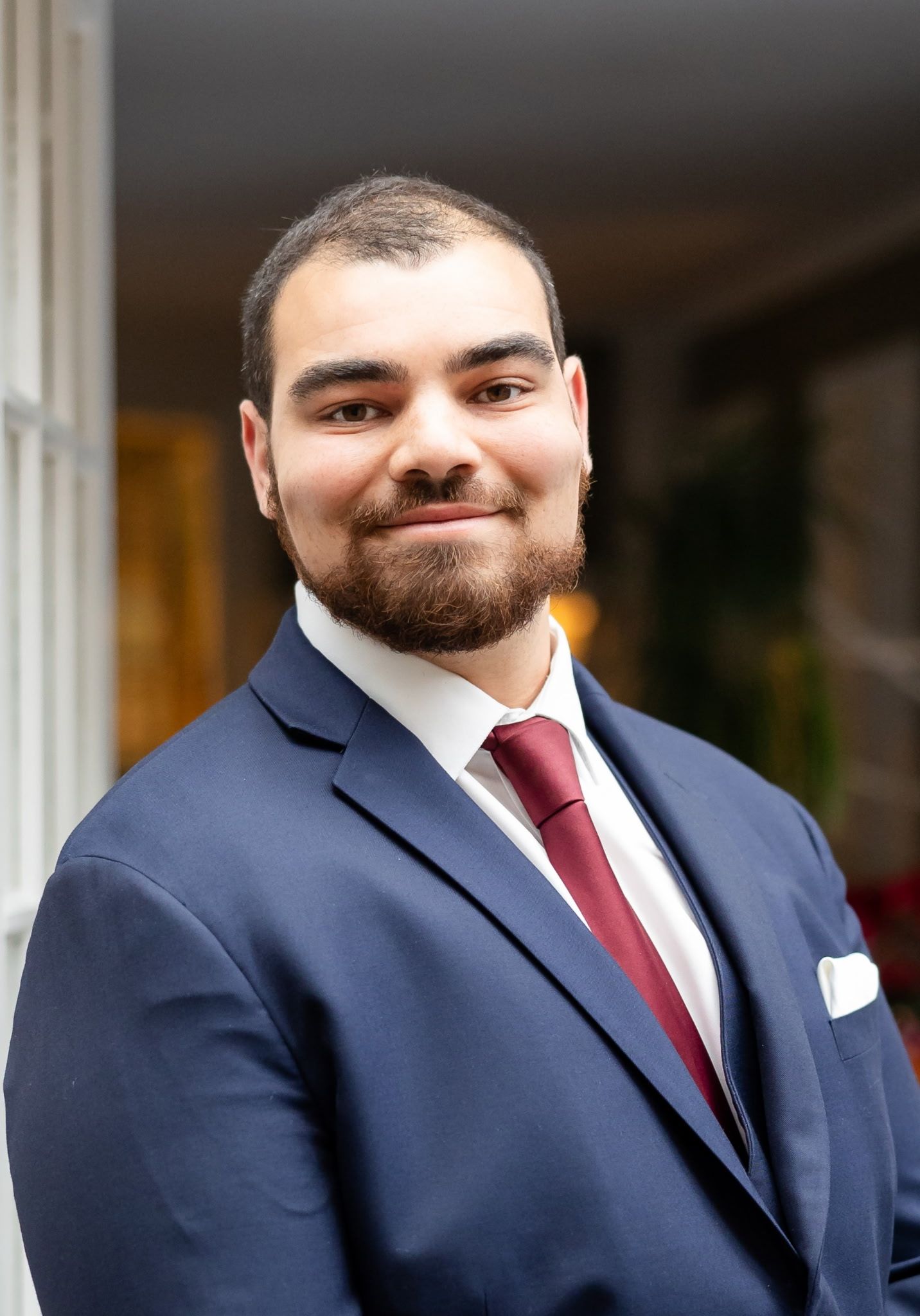Professional headshot of a person wearing a navy suit and burgundy tie with a friendly smile.