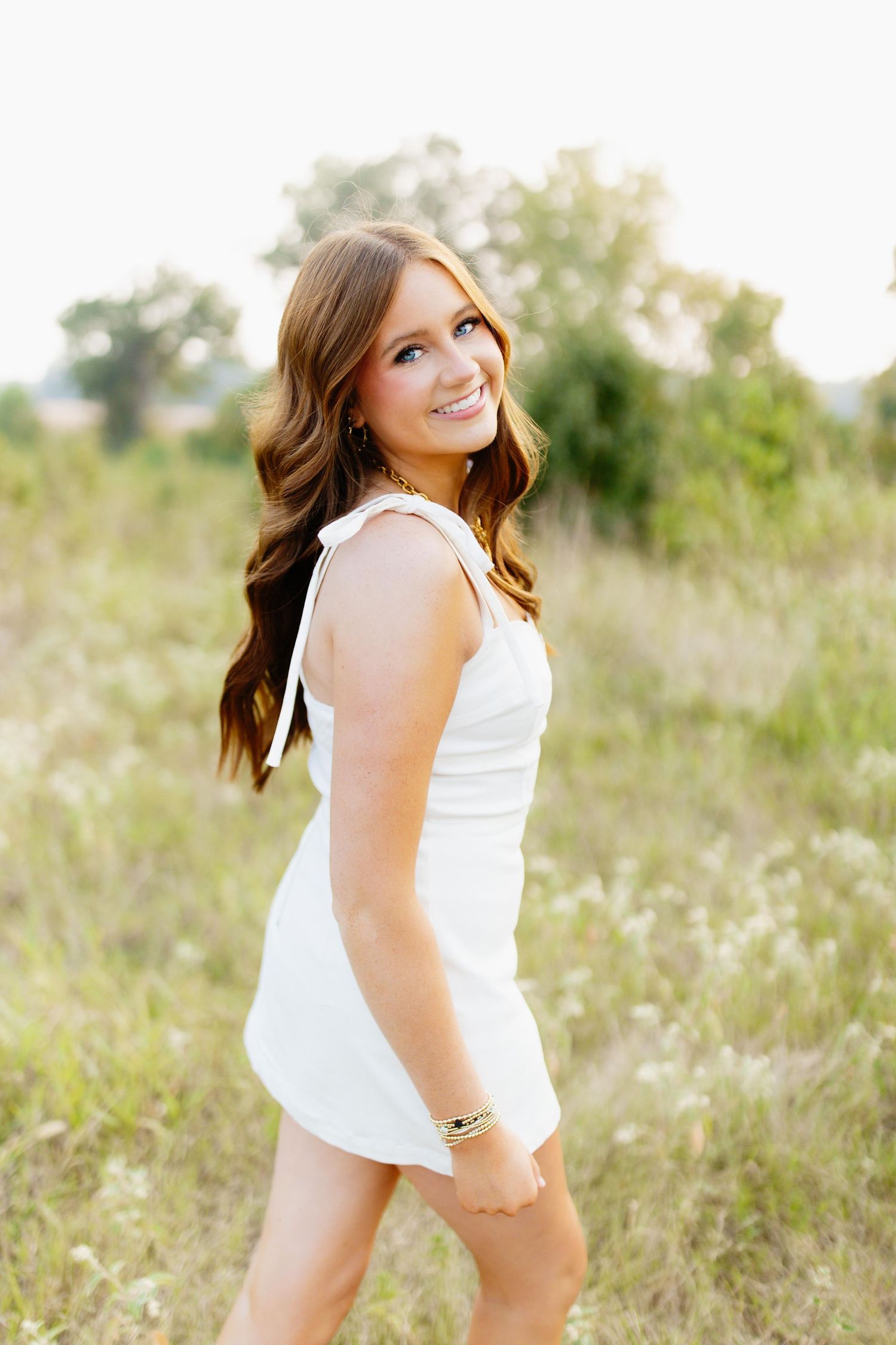 Side view portrait in a white summer dress standing in a sunlit meadow with flowing hair.