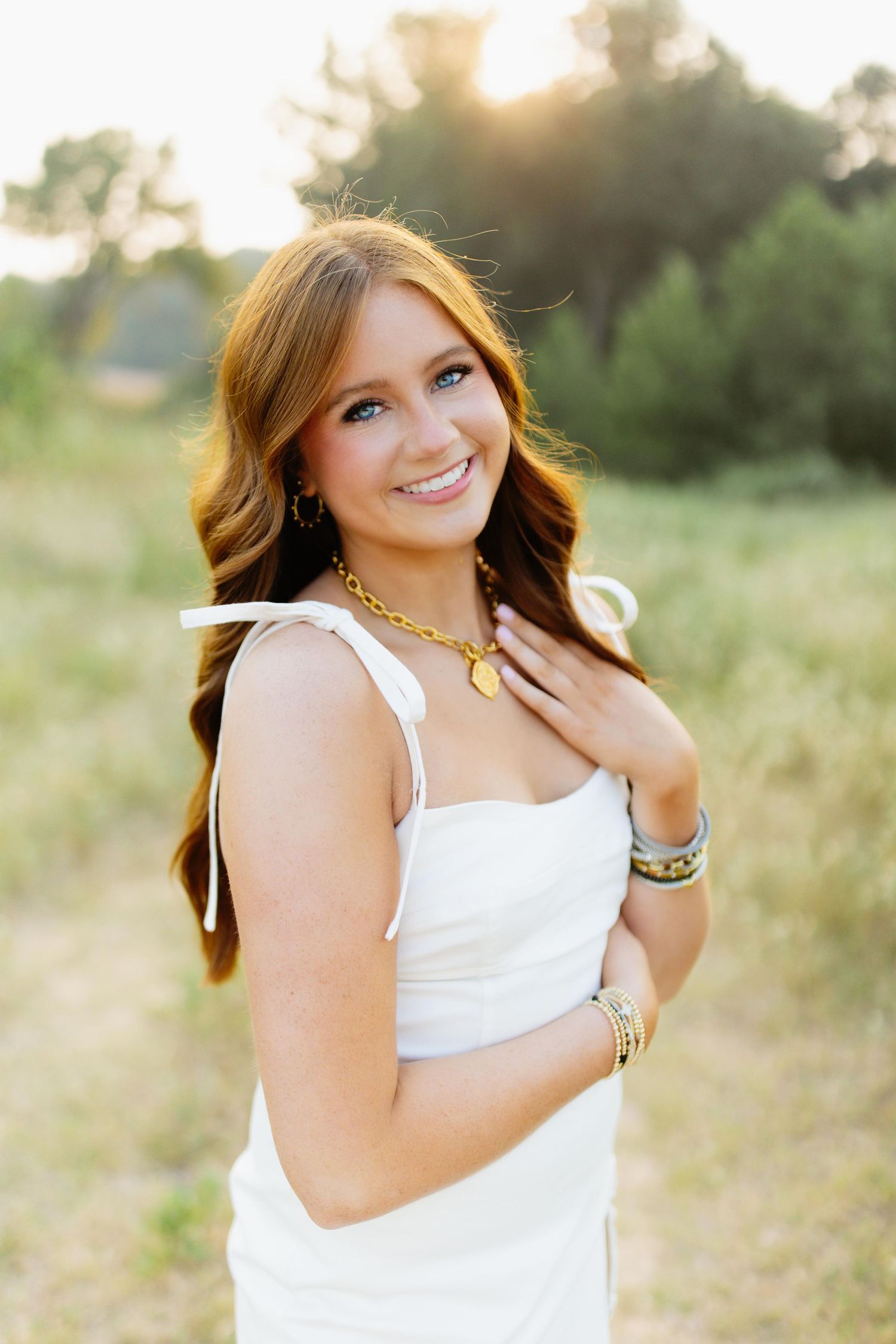 Sunset portrait wearing a white dress and gold necklace while posing in a natural outdoor setting.