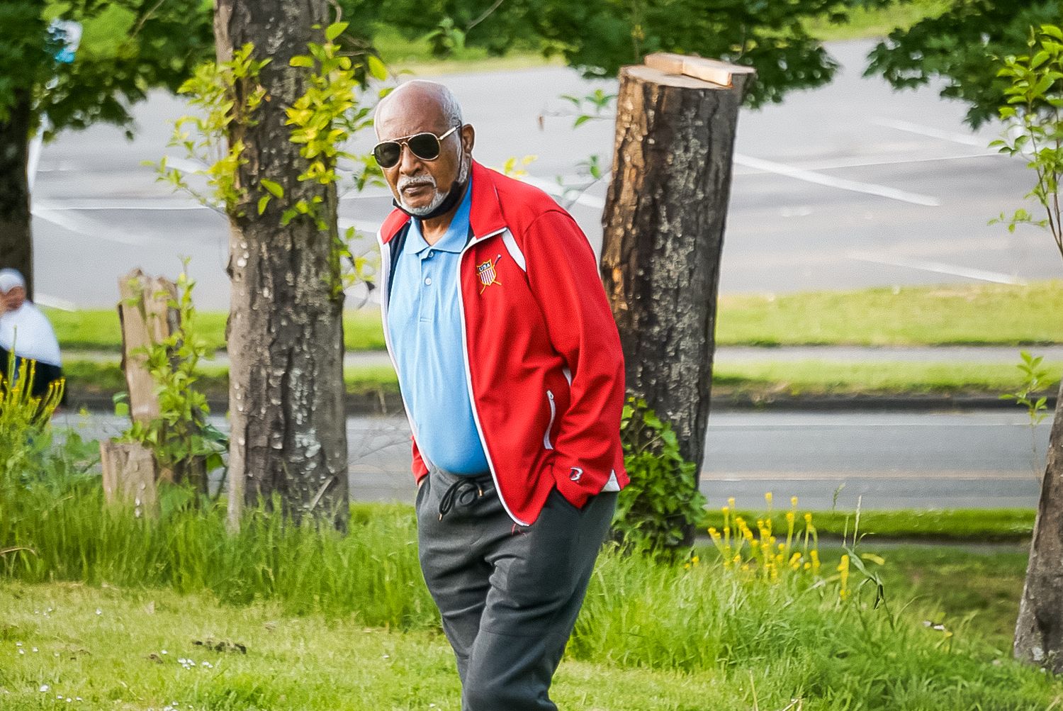 Active senior wearing red jacket and glasses enjoys a sunny day outdoors in a park setting.