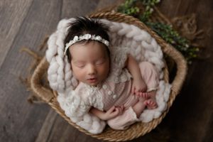 Newborn photography of a baby swaddled in soft white blankets sleeping peacefully in a woven basket.