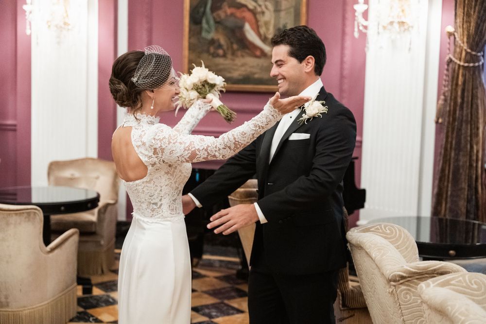 A couple shares their first dance in an elegant pink-walled ballroom setting.