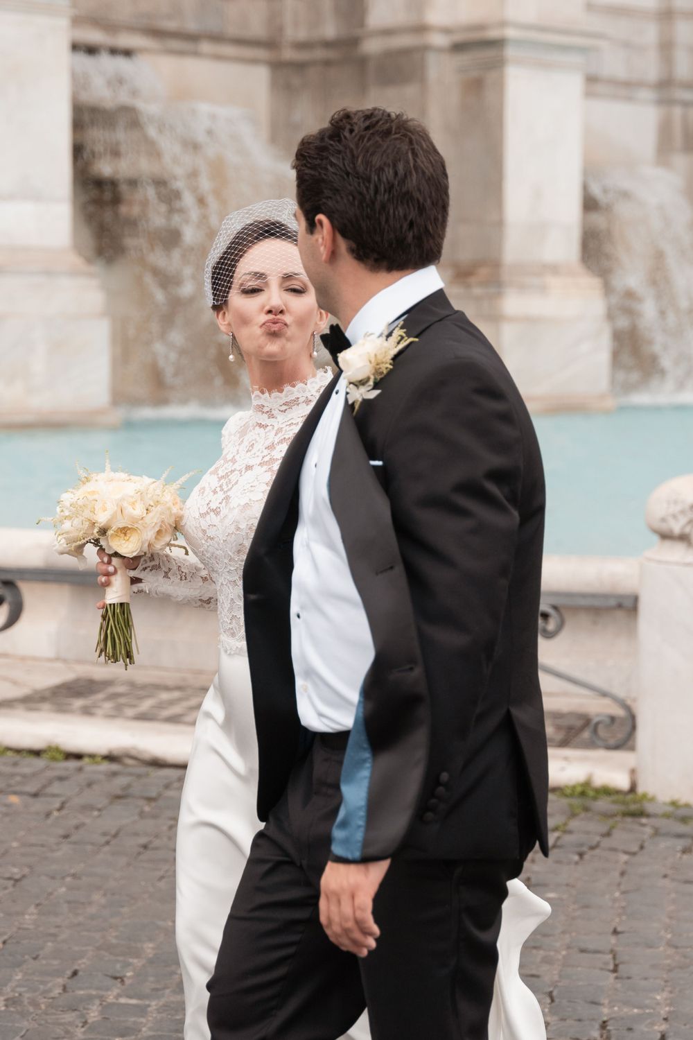 A couple shares a joyful moment during their wedding photoshoot by historic stone columns.
