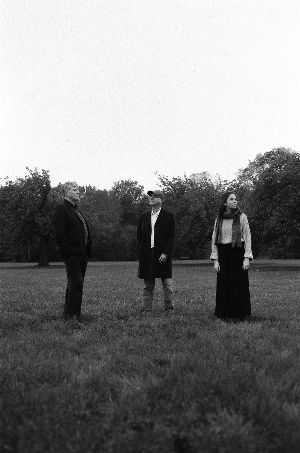 Three figures stand in a field at dusk in this black and white vintage photograph.