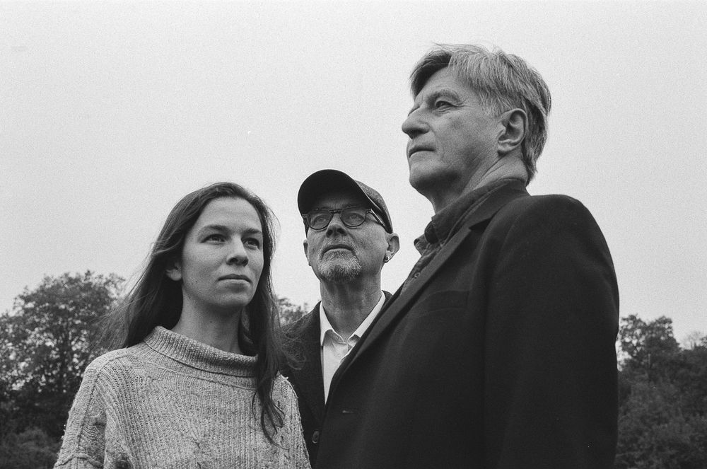 A black and white portrait of three people standing together outdoors looking off into the distance.