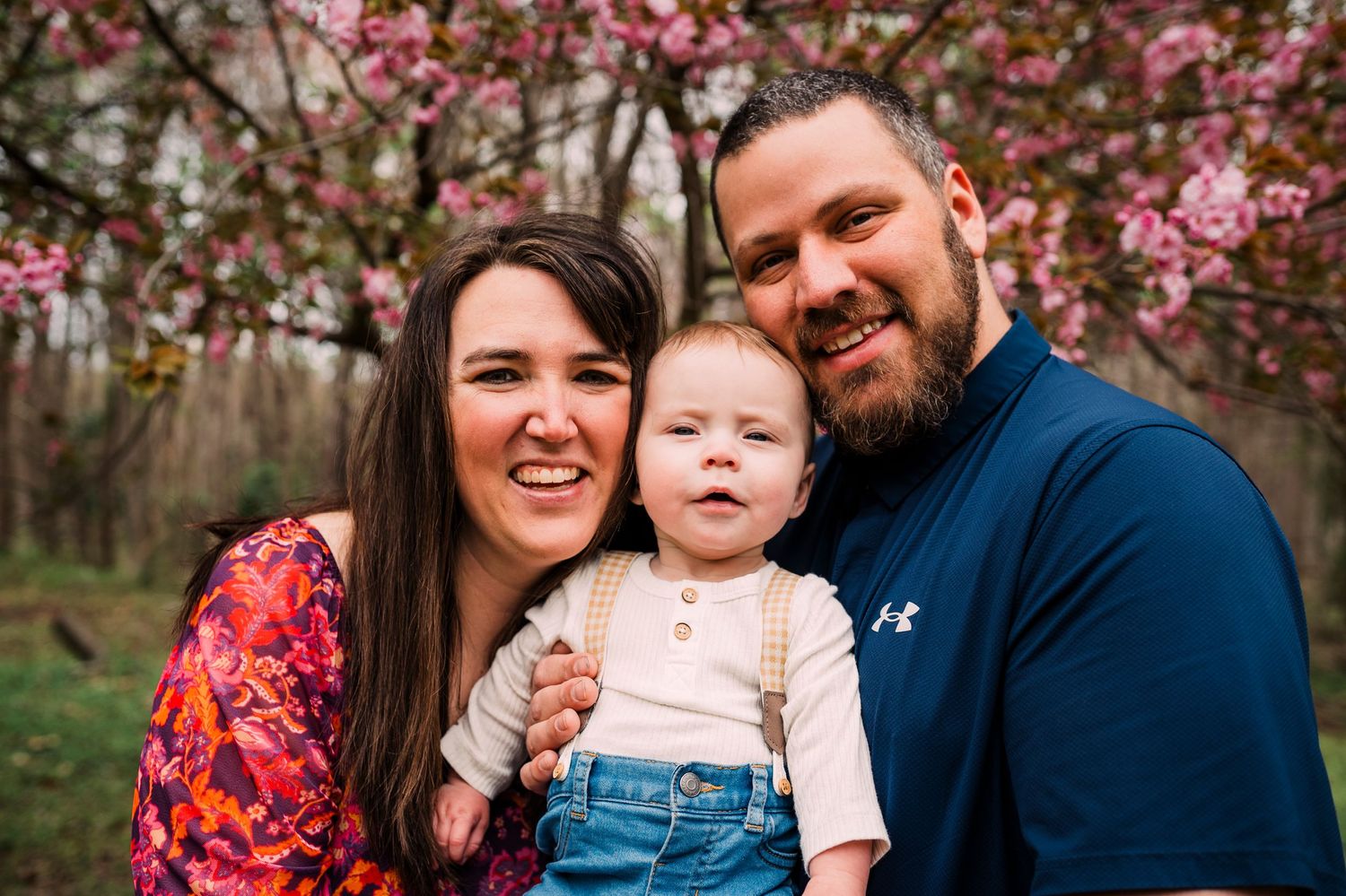 Family enjoying spring photo session under blooming pink cherry blossom trees in the outdoors.
