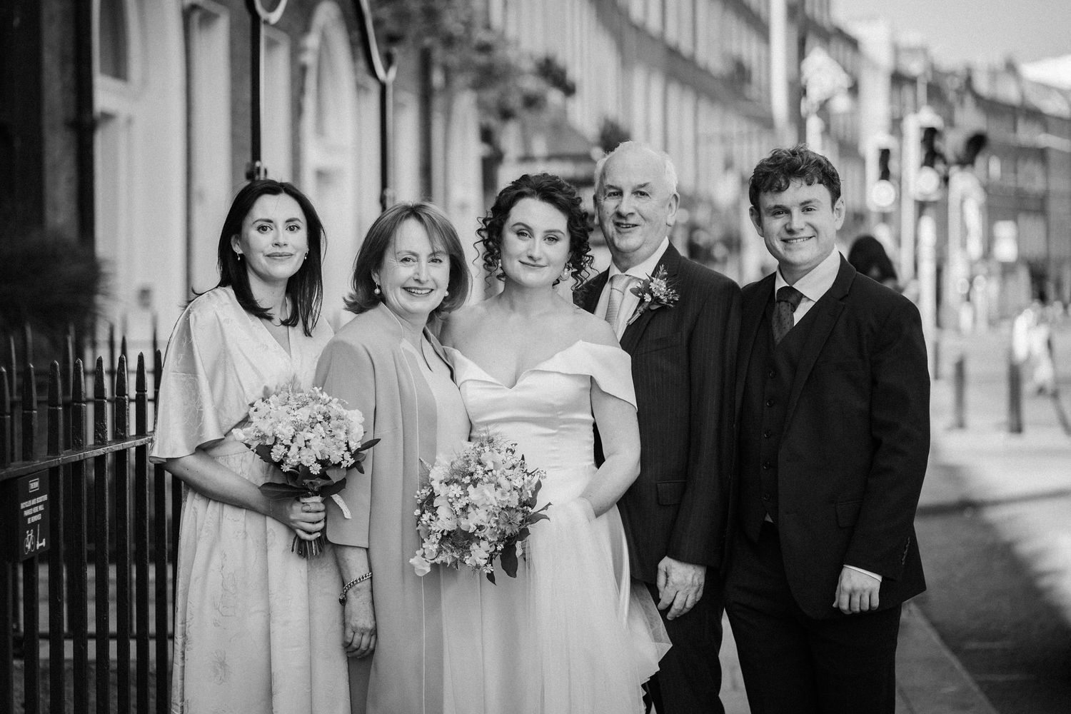 Black and white photo of a wedding party standing together on a city street holding floral bouquets.