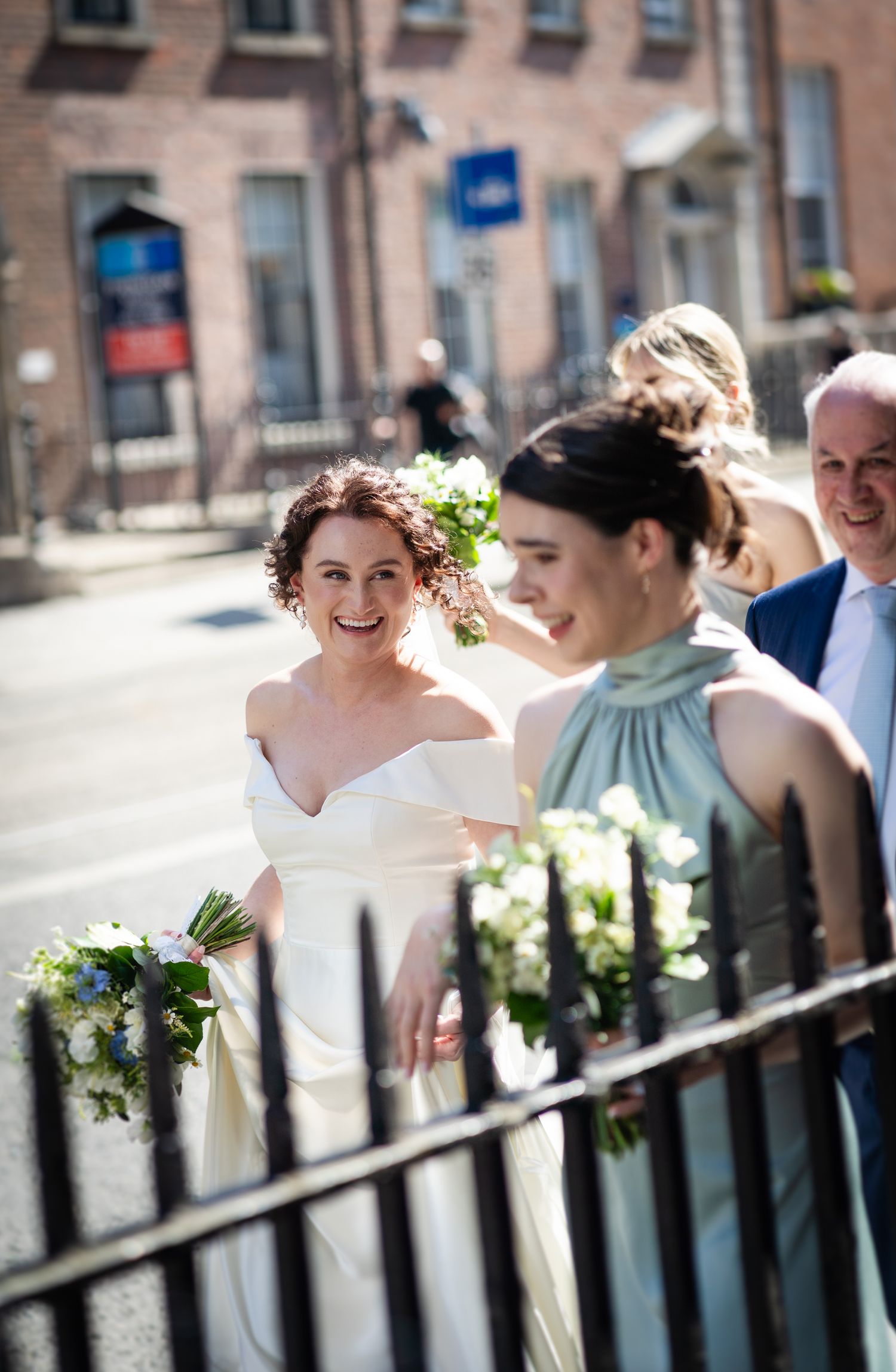 Wedding party walks down a sunny city street with bridesmaids in mint dress carrying white bouquets.