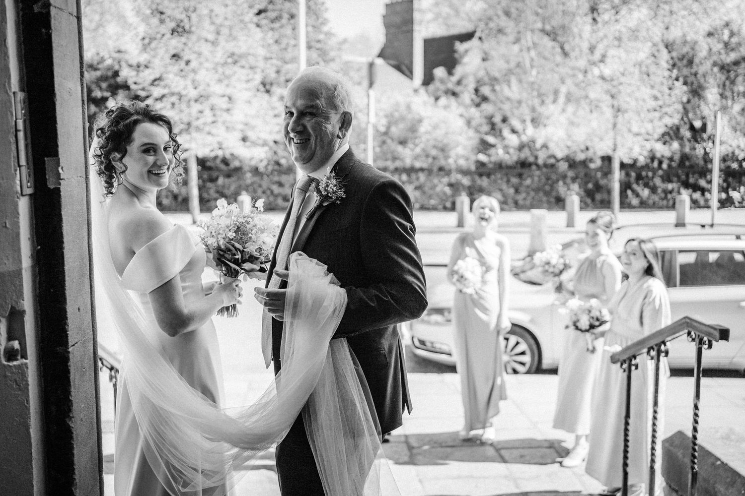 A bride shares a happy moment with a guest outside a venue in black and white photography.