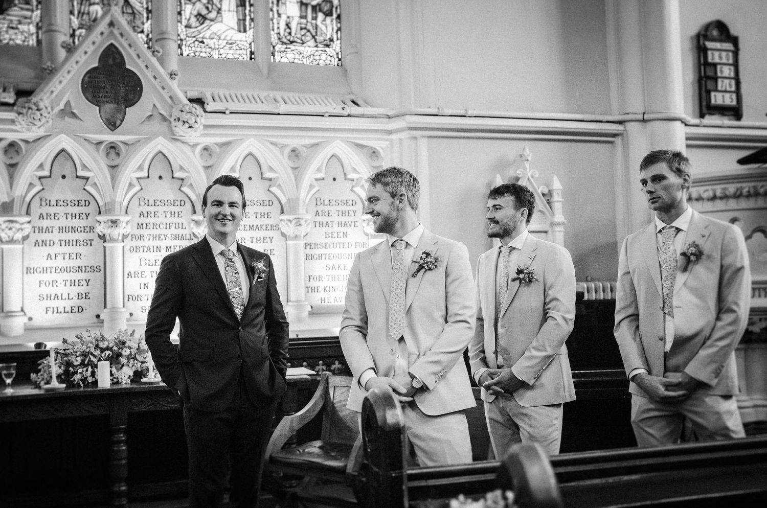 Black and white photograph showing a wedding party of four men in formal attire standing at the altar in a church.
