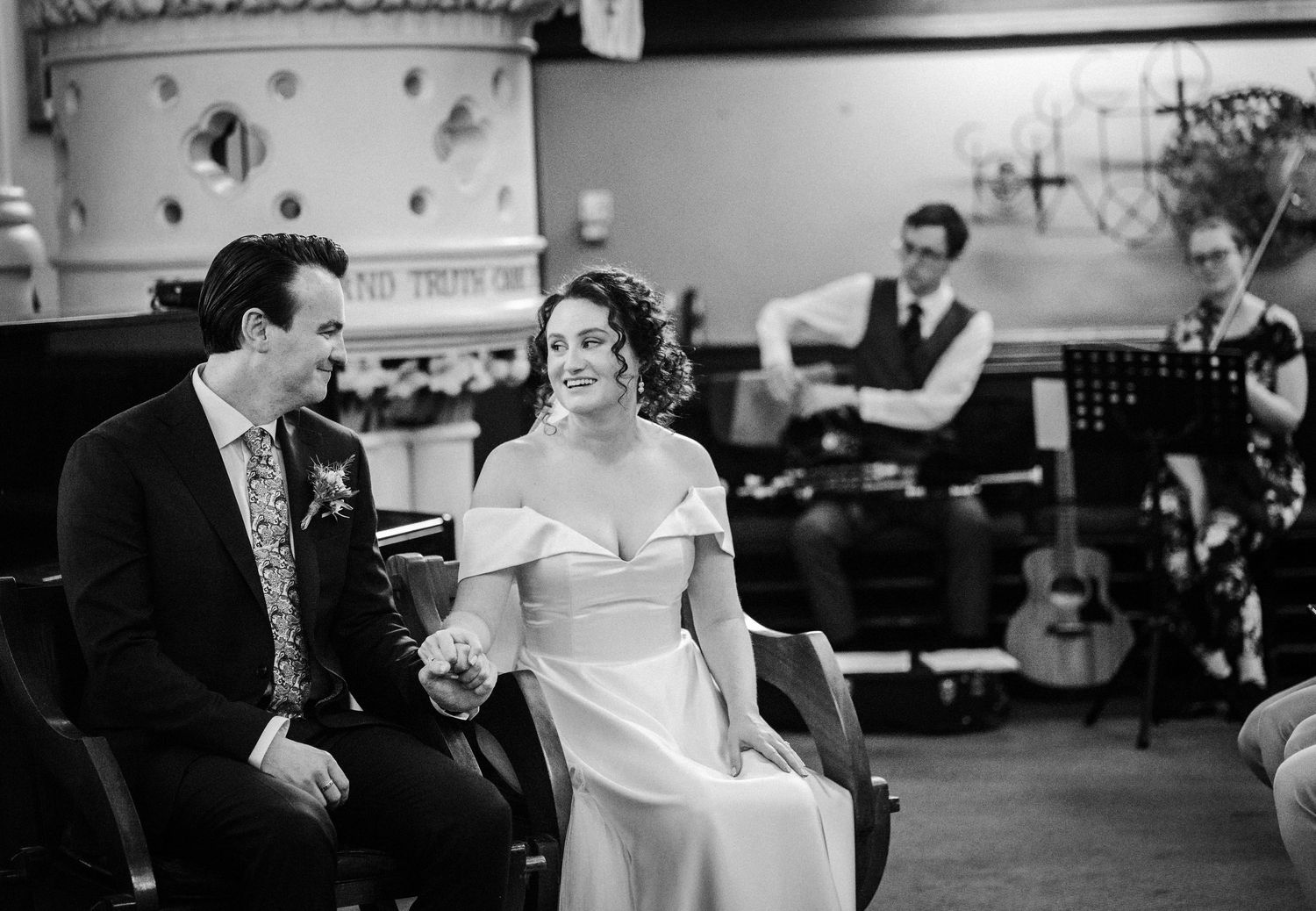 A couple shares a joyful moment at their wedding reception with musicians visible in the background.