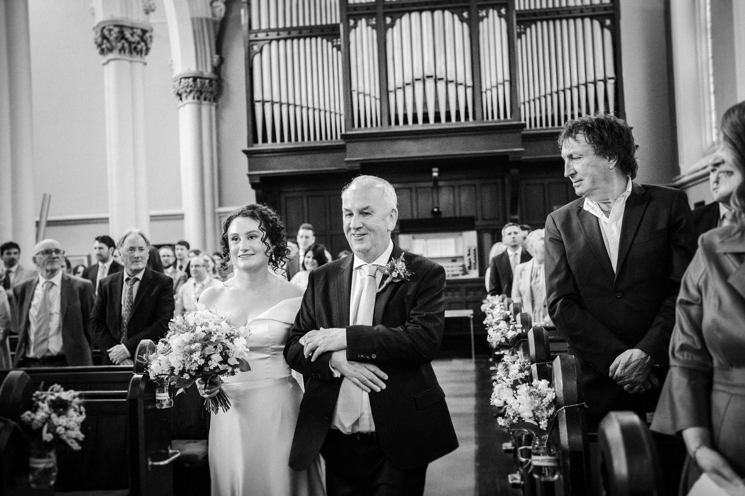 Black and white photo of a wedding ceremony in a traditional church with an elegant organ pipe backdrop.