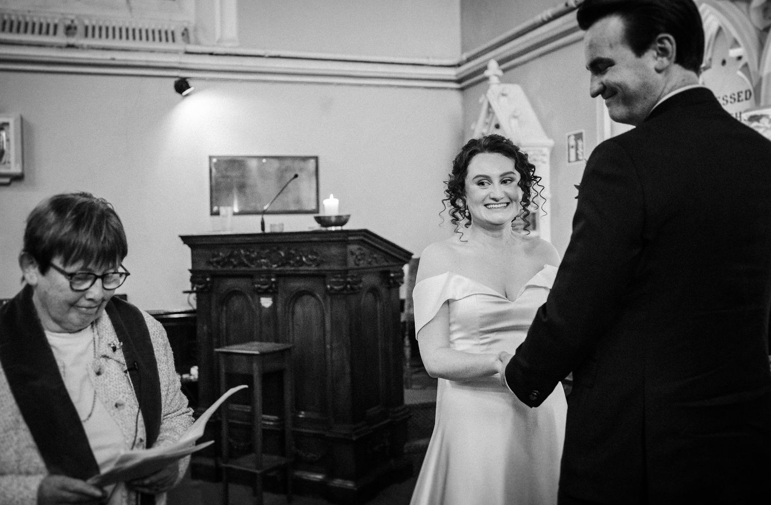 A vintage black and white photograph showing three people during what appears to be a wedding ceremony indoors.