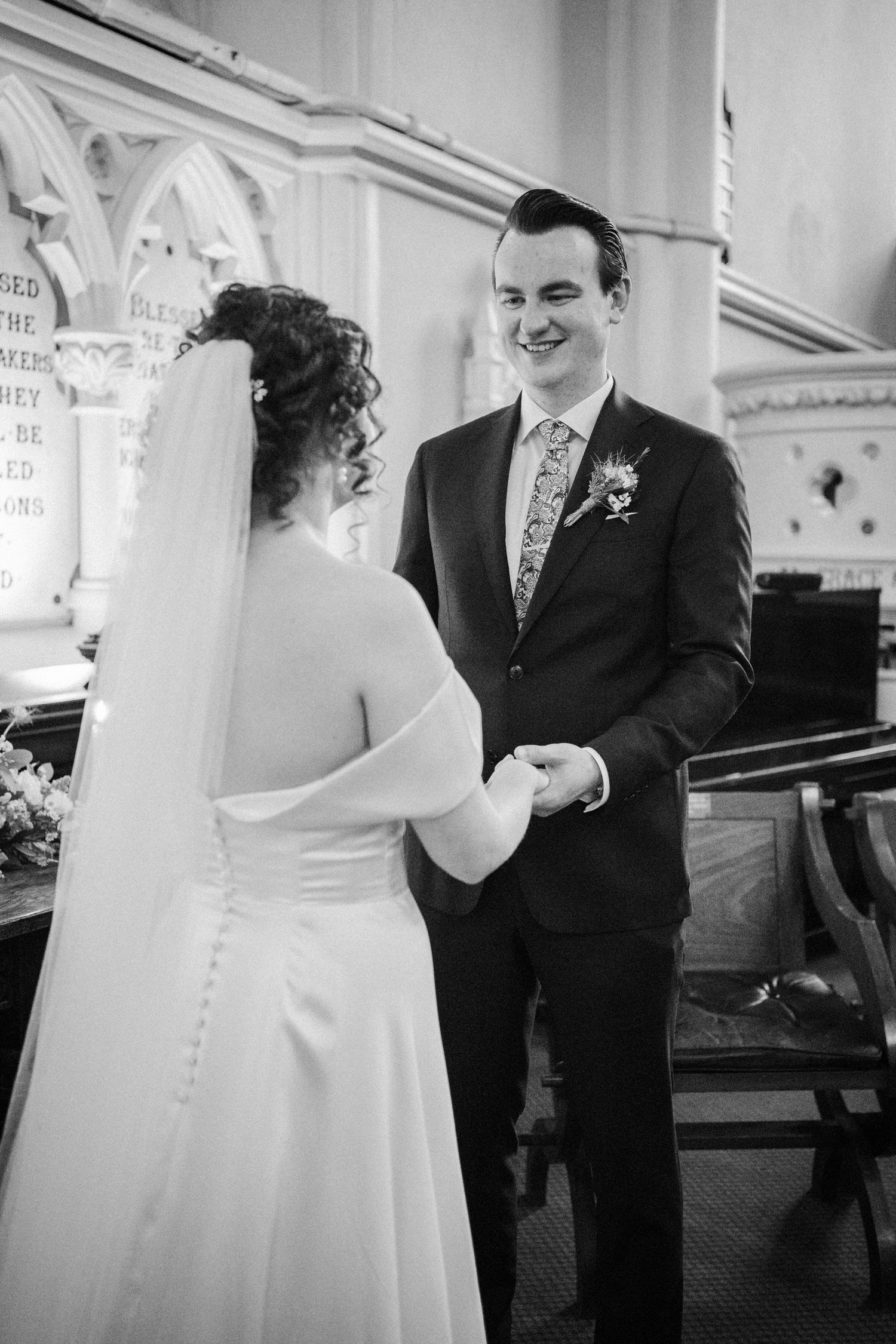 A black and white photograph of a couple during their wedding ceremony exchanging vows in a church altar area.