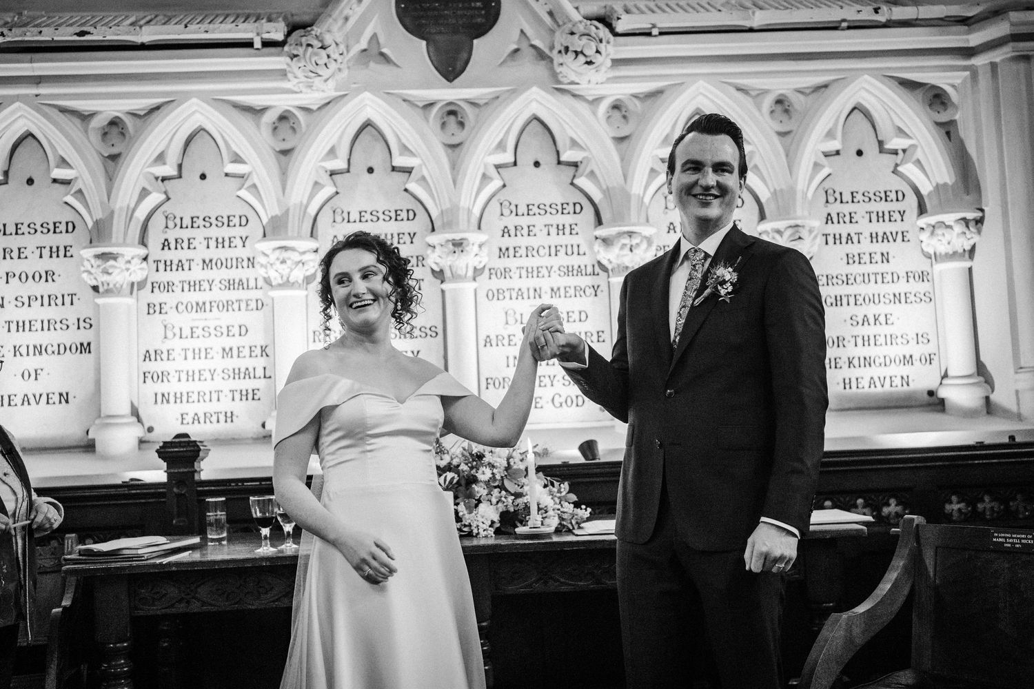 A joyful black and white photo of a couple sharing a celebratory moment at their wedding ceremony in front of ornate carvings.
