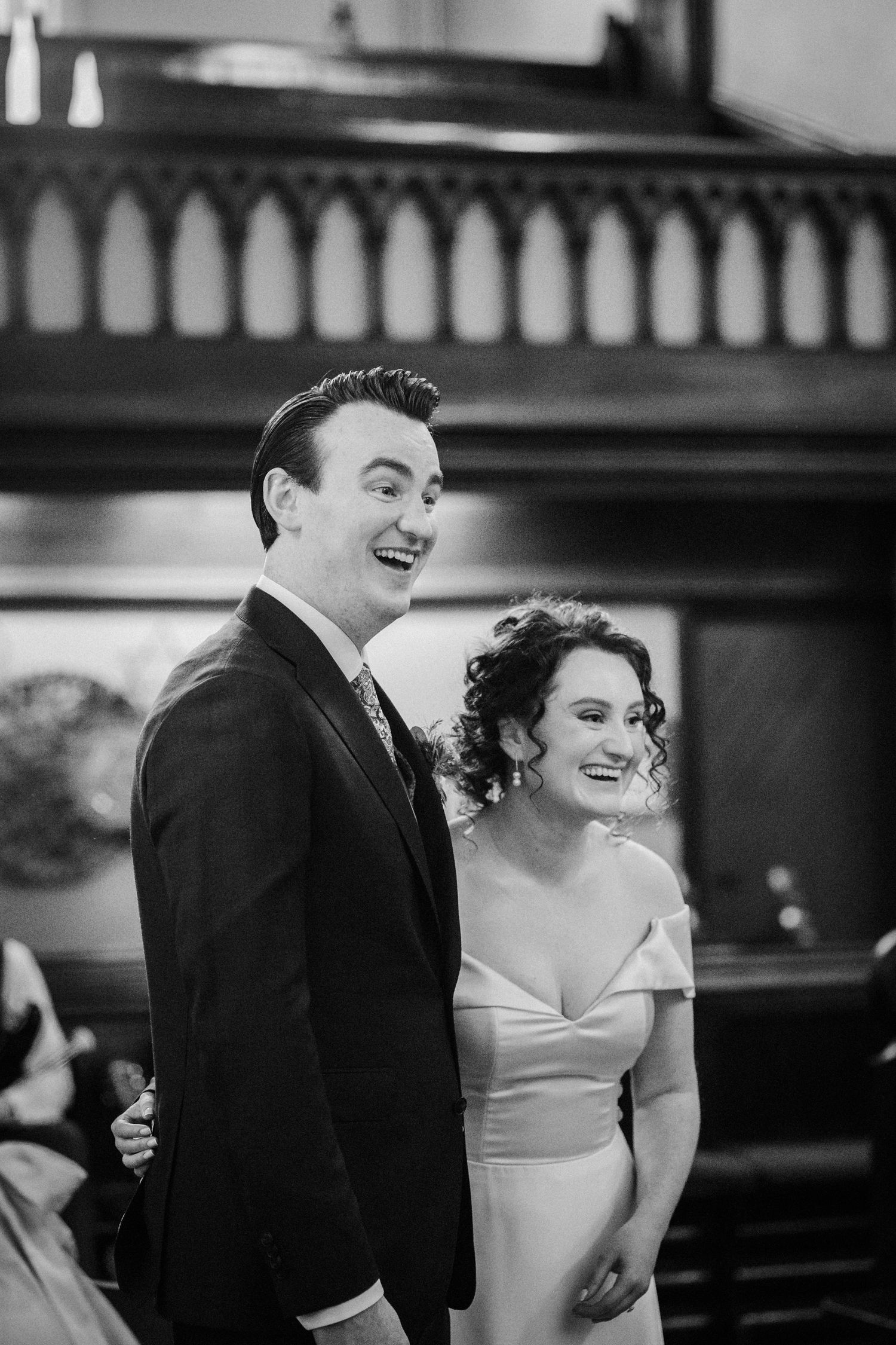 A black and white candid wedding photo of a joyful couple laughing together during their ceremony.