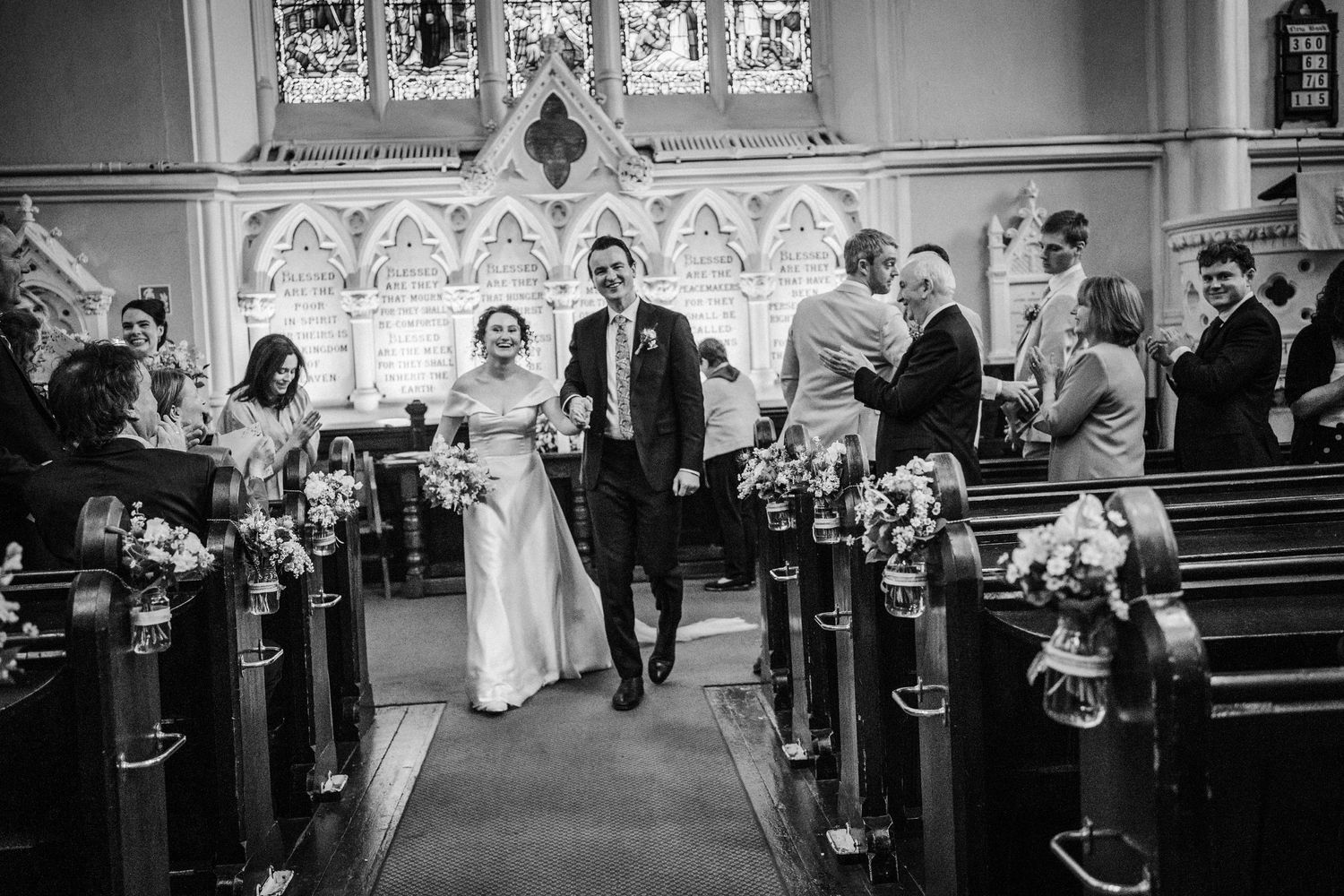 A joyful couple walks down the church aisle after their wedding ceremony while guests look on from the pews.
