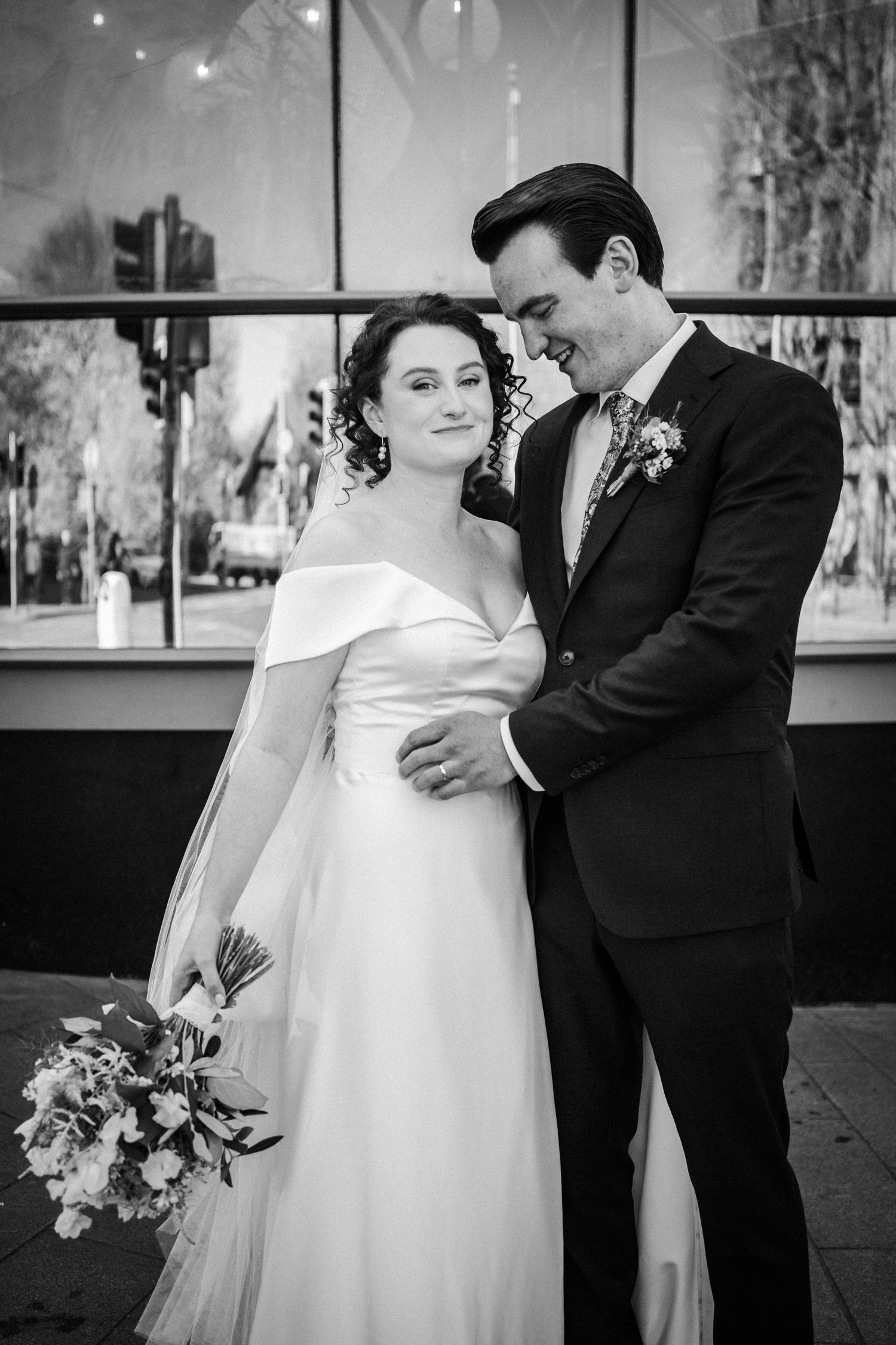 Elegant black and white wedding photograph of a romantic couple sharing an intimate moment with a floral bouquet.