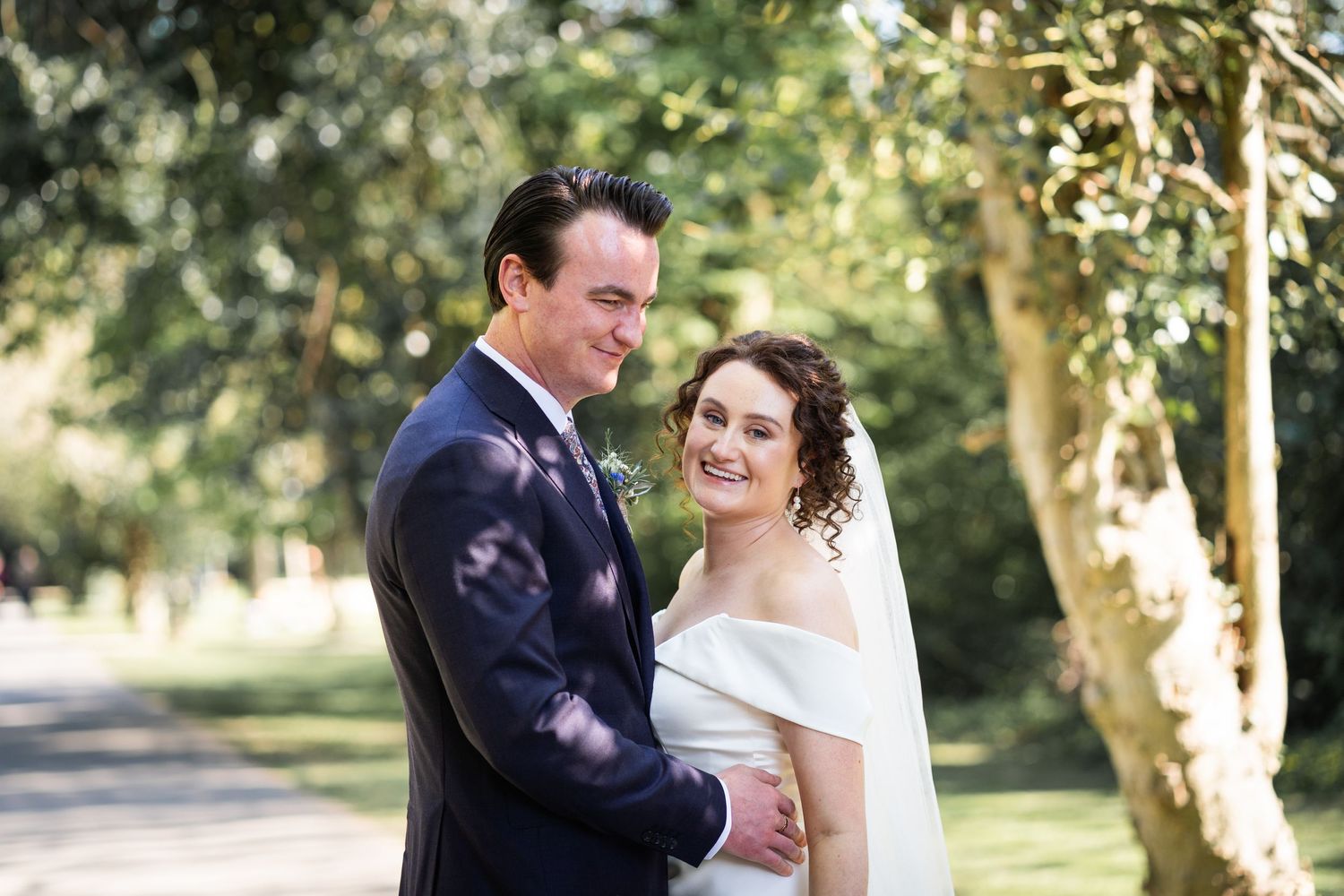 A bride and groom share a romantic moment together outdoors on a tree-lined path during their wedding day.