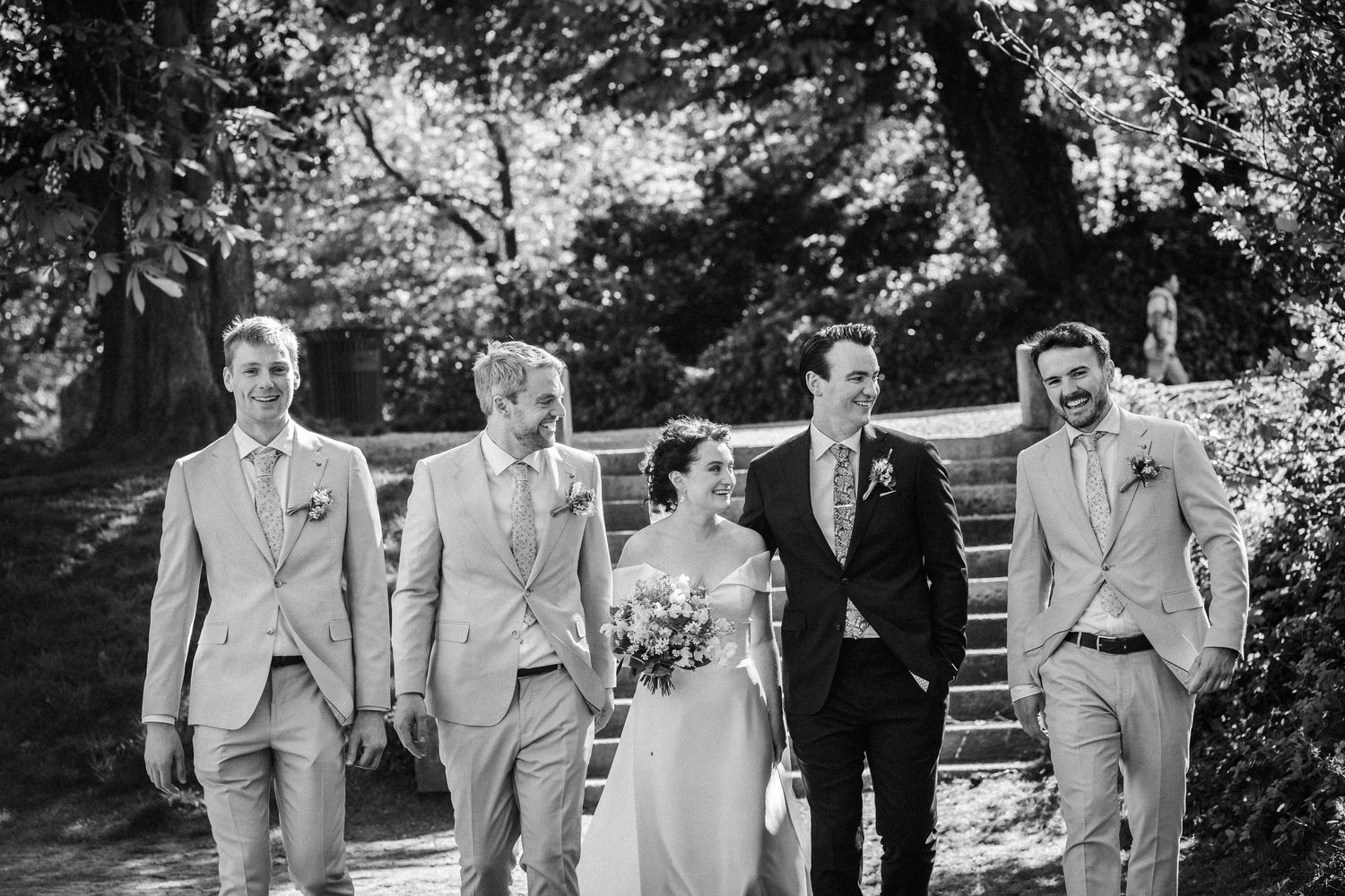 Black and white photo of a wedding party walking together on garden steps in coordinated formal attire.