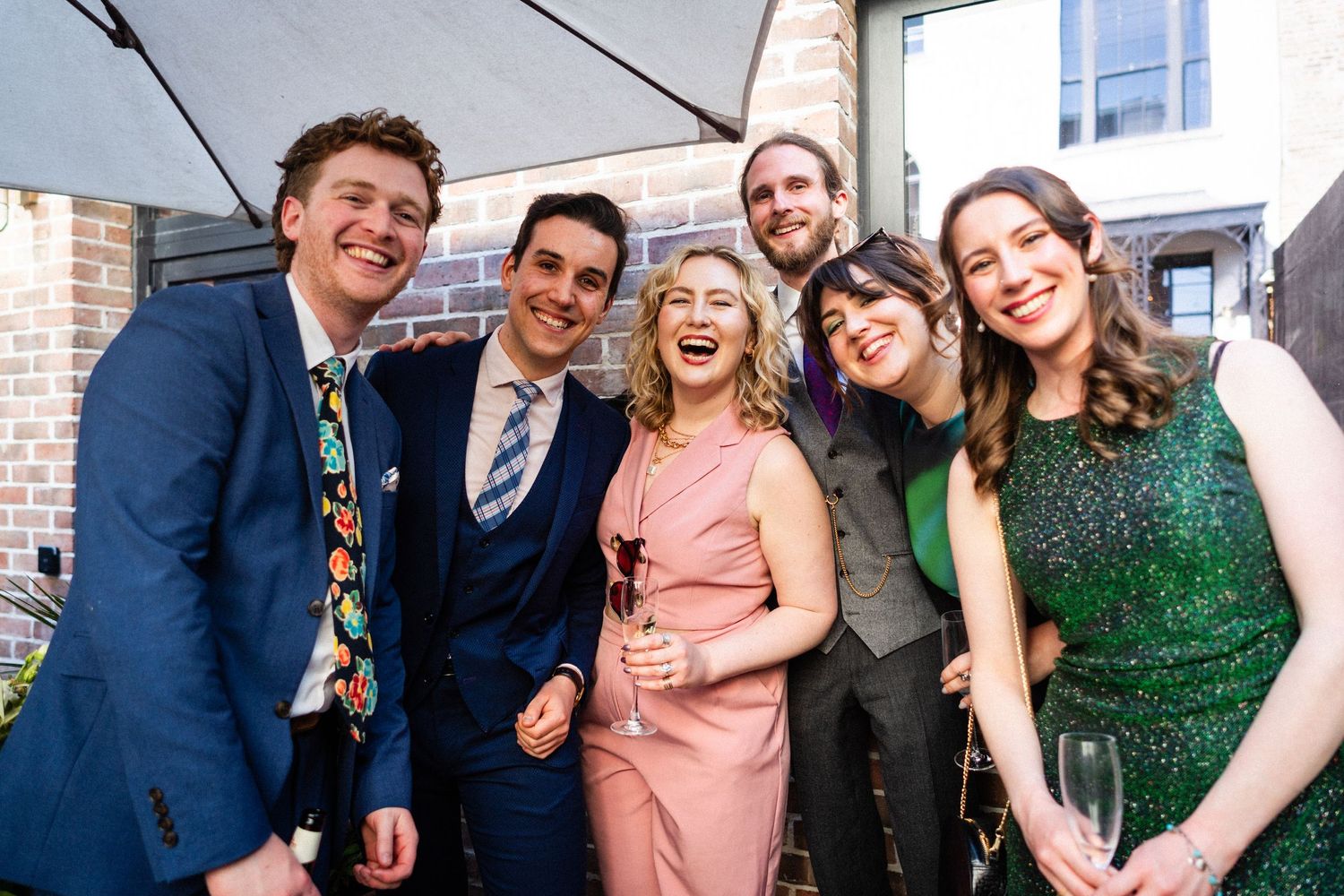 A cheerful group of well-dressed friends share a candid laughing moment together at a formal event.