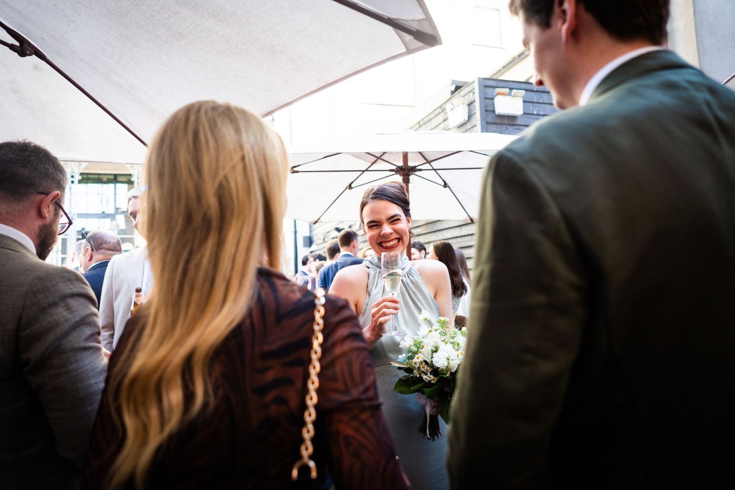 Wedding celebration gathering under white umbrellas with guests mingling at an outdoor venue.