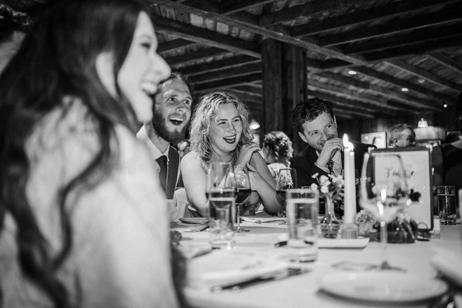 Black and white candid photo of people laughing together while dining at a dinner party.