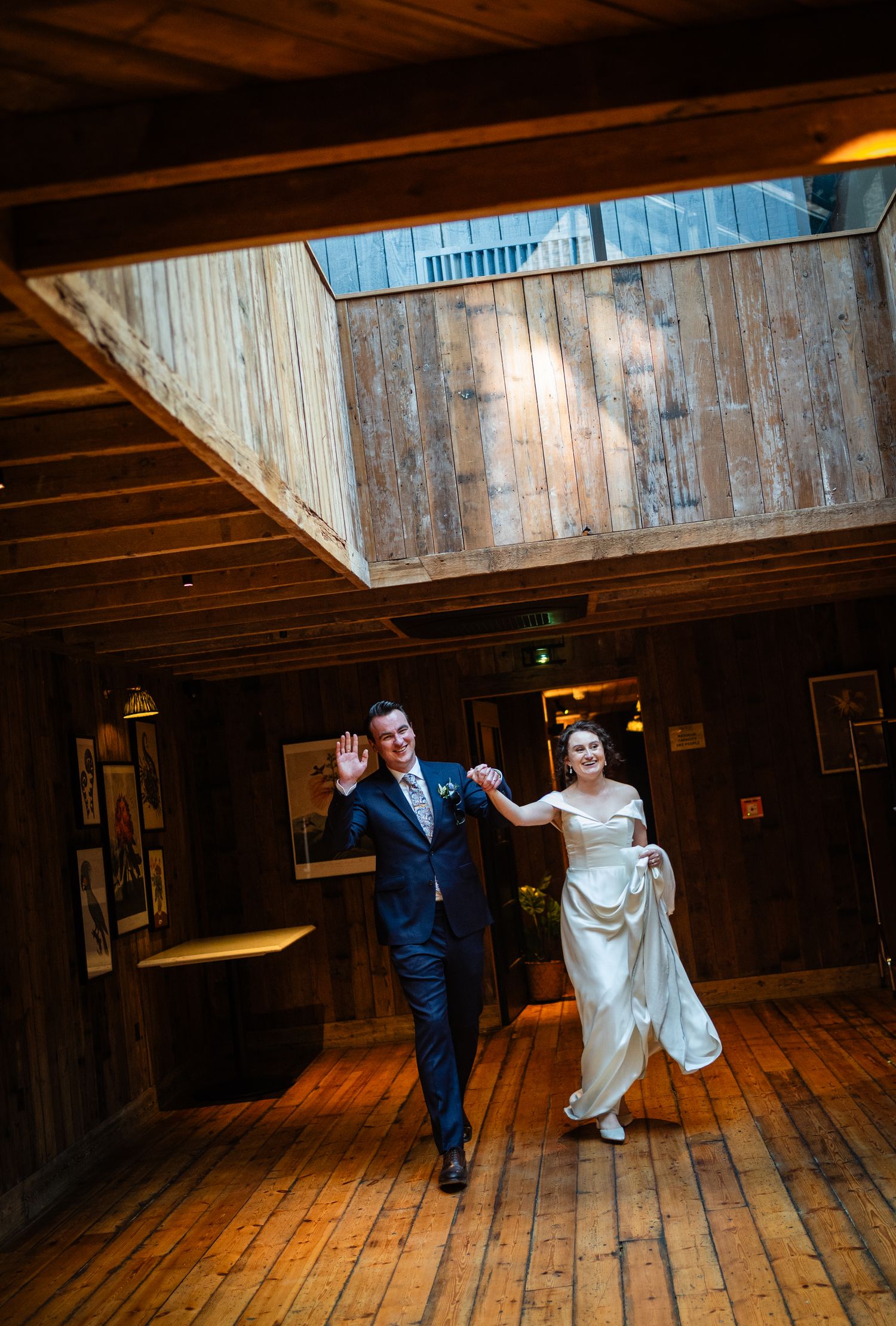 A couple dances joyfully together in a rustic wooden venue with natural light streaming through a skylight above.