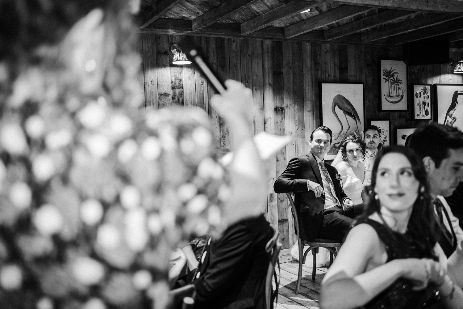 A black and white photograph shows patrons seated at a dimly lit bar with artwork on the walls in the background.