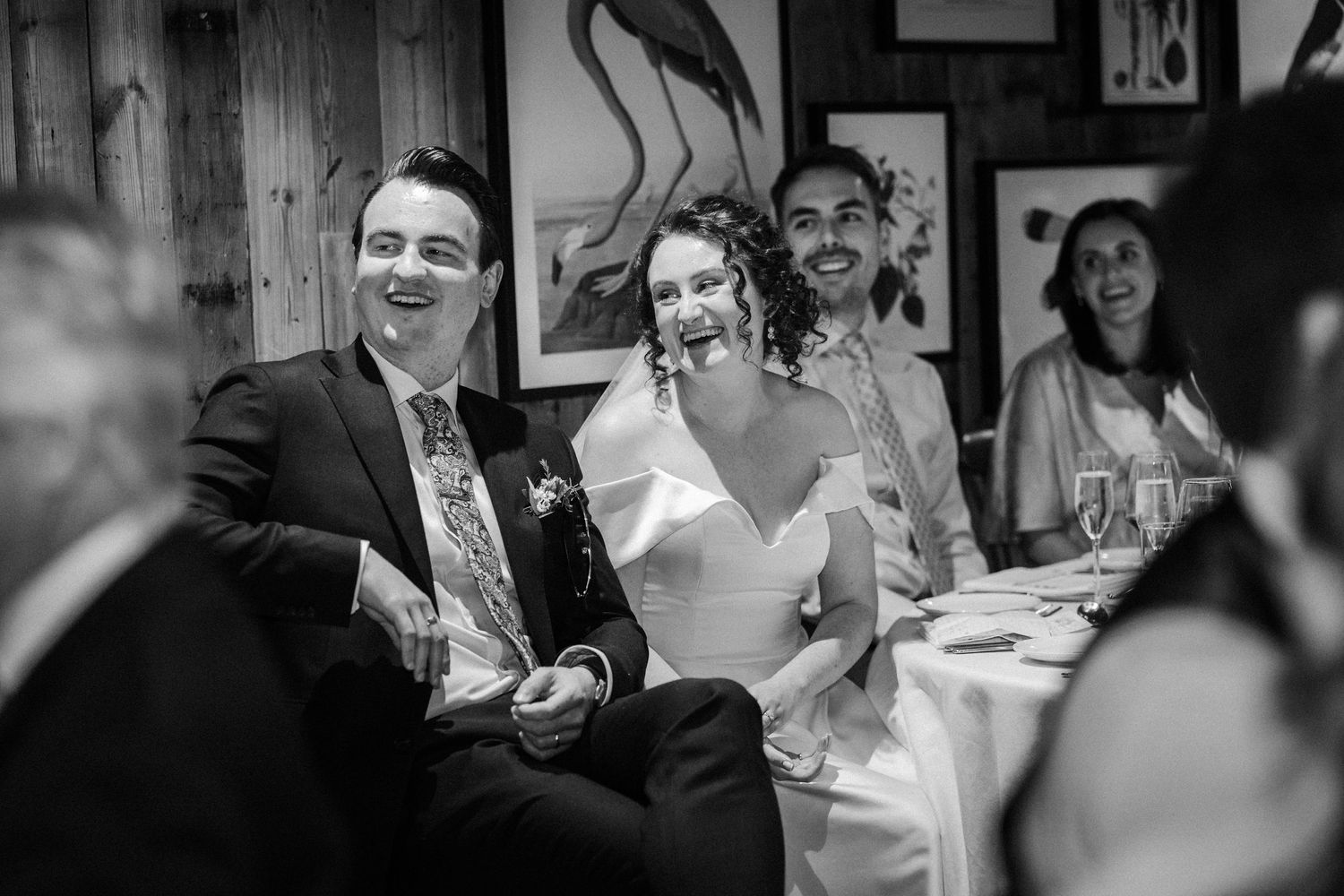 Black and white candid photograph of a wedding couple laughing during a reception celebration.