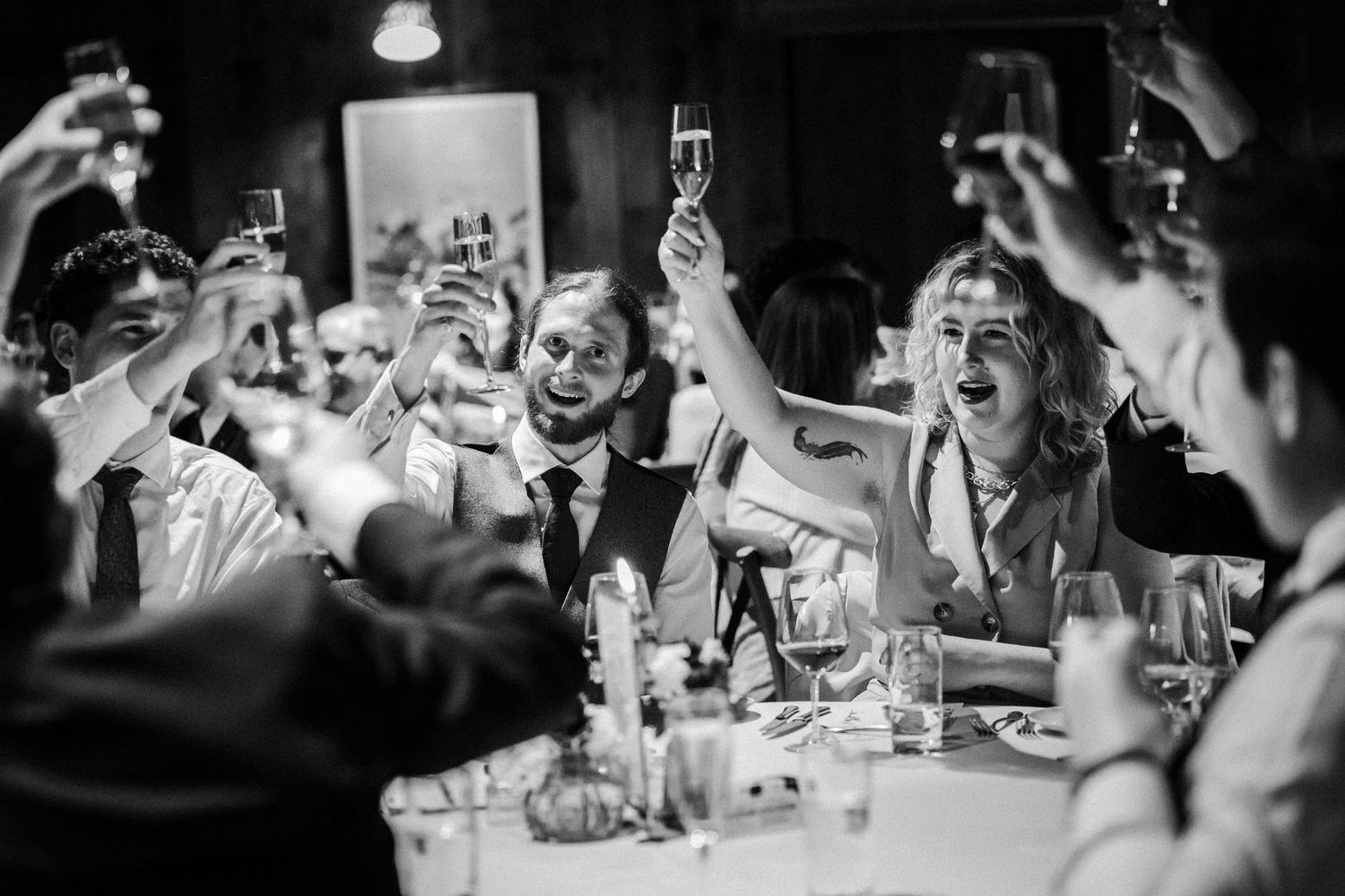A lively black and white party scene shows guests raising champagne glasses in celebration at a dinner table.