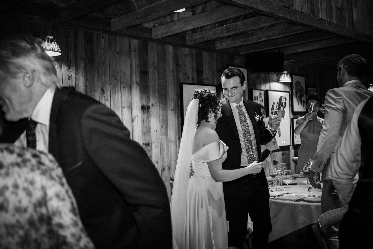 A couple shares a tender moment during their wedding reception in a rustic wooden barn venue captured in black and white.