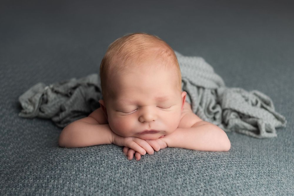Peaceful sleeping newborn rests on gray blanket in professional studio portrait setup.