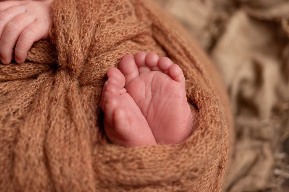 Tiny newborn baby foot wrapped in cozy brown knit blanket in soft lighting.