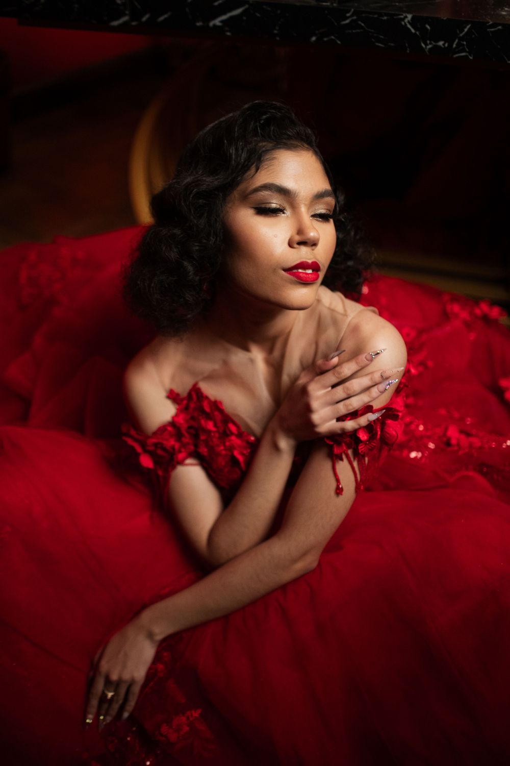 Glamorous portrait in a flowing red dress against dark background with dramatic lighting and vintage-inspired styling.