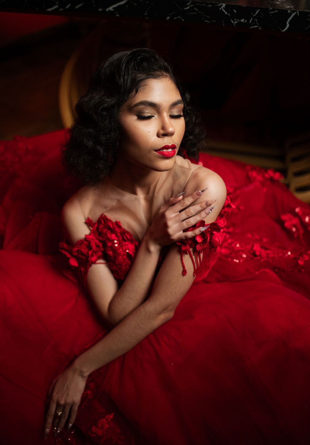 A glamorous portrait in a flowing red gown with vintage-inspired curls and classic red lipstick against a dark backdrop.
