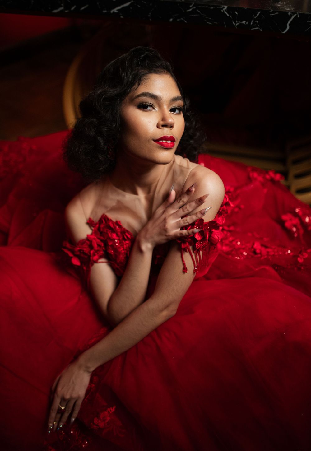 A glamorous vintage-inspired photoshoot featuring a red ball gown with delicate lace details in moody lighting.