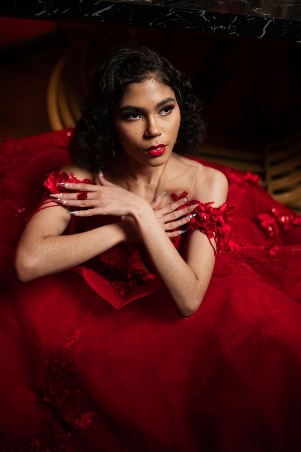 Elegant portrait in a luxurious red dress with retro-styled curls against a dark background.