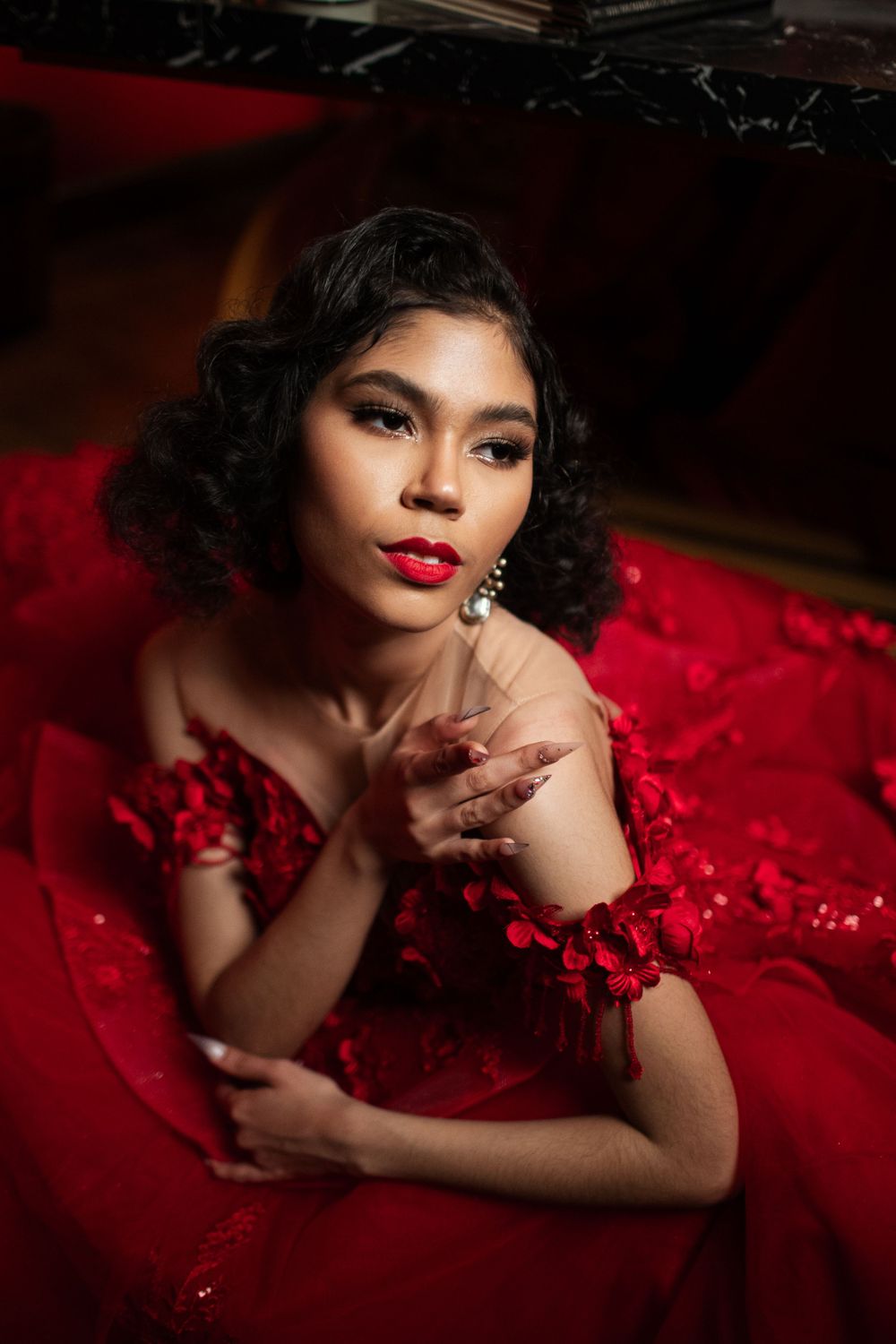 Glamorous portrait in red evening gown with vintage-style curls, bold red lipstick, and dramatic lighting against dark background.