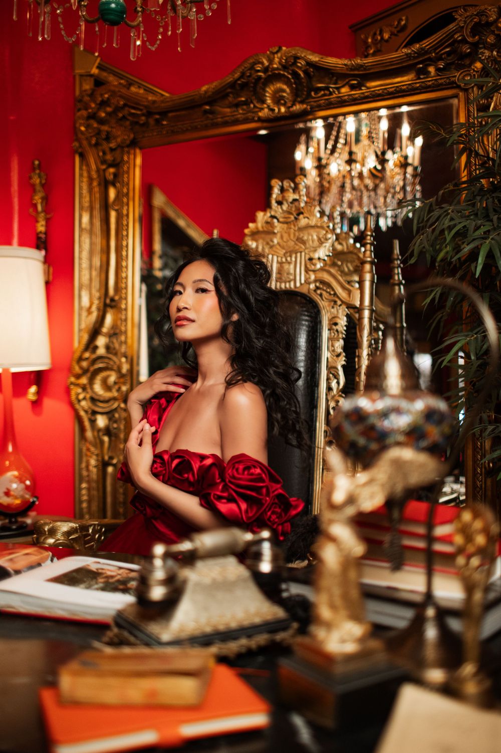 Luxurious boudoir scene with crystal chandelier, ornate gold mirror, and red walls creating romantic ambiance.